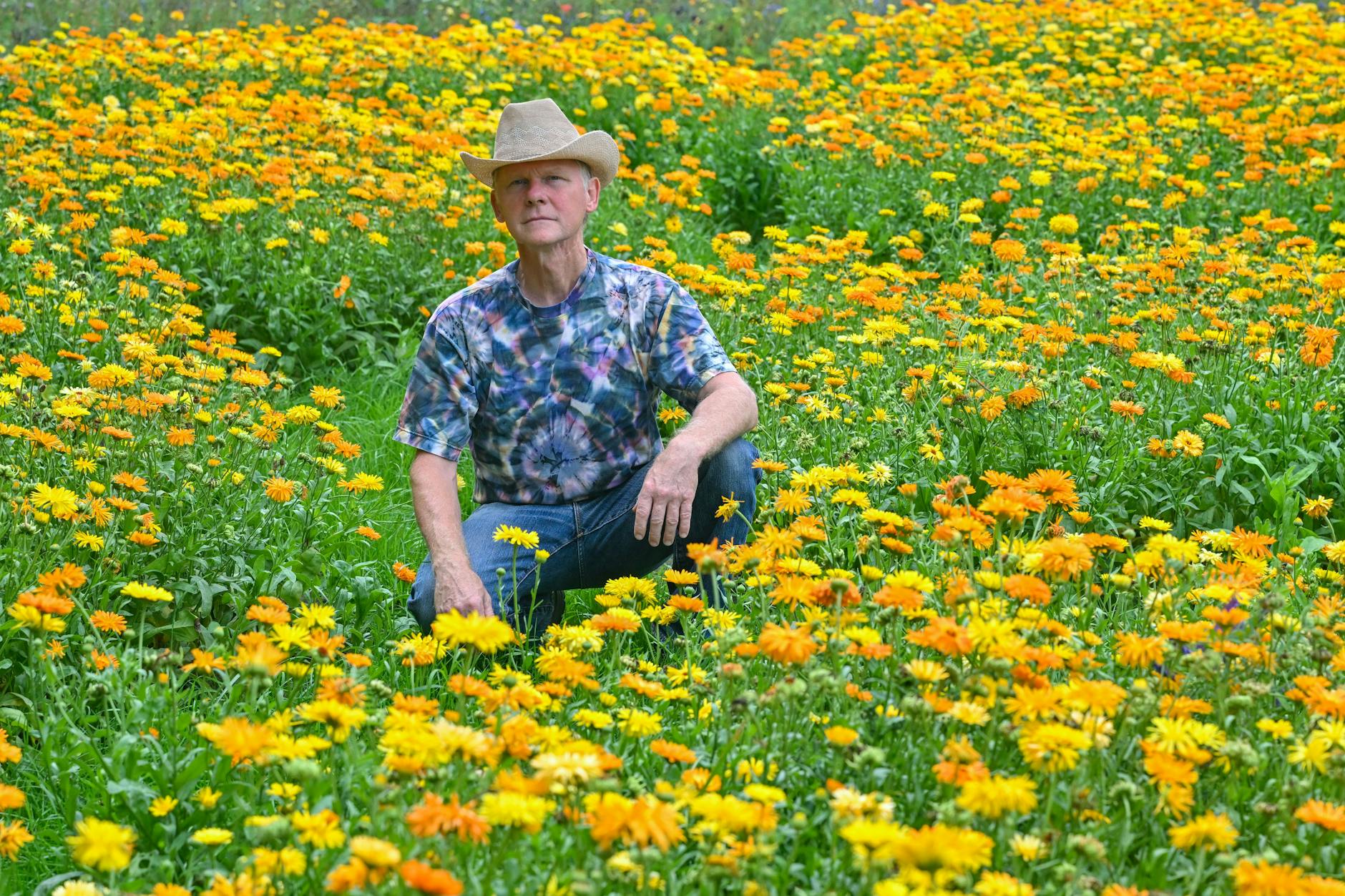 Künstler Michael Uy hockt zwischen blühenden Ringelblumen auf seiner ganz besonderen Wiese für Insekten.