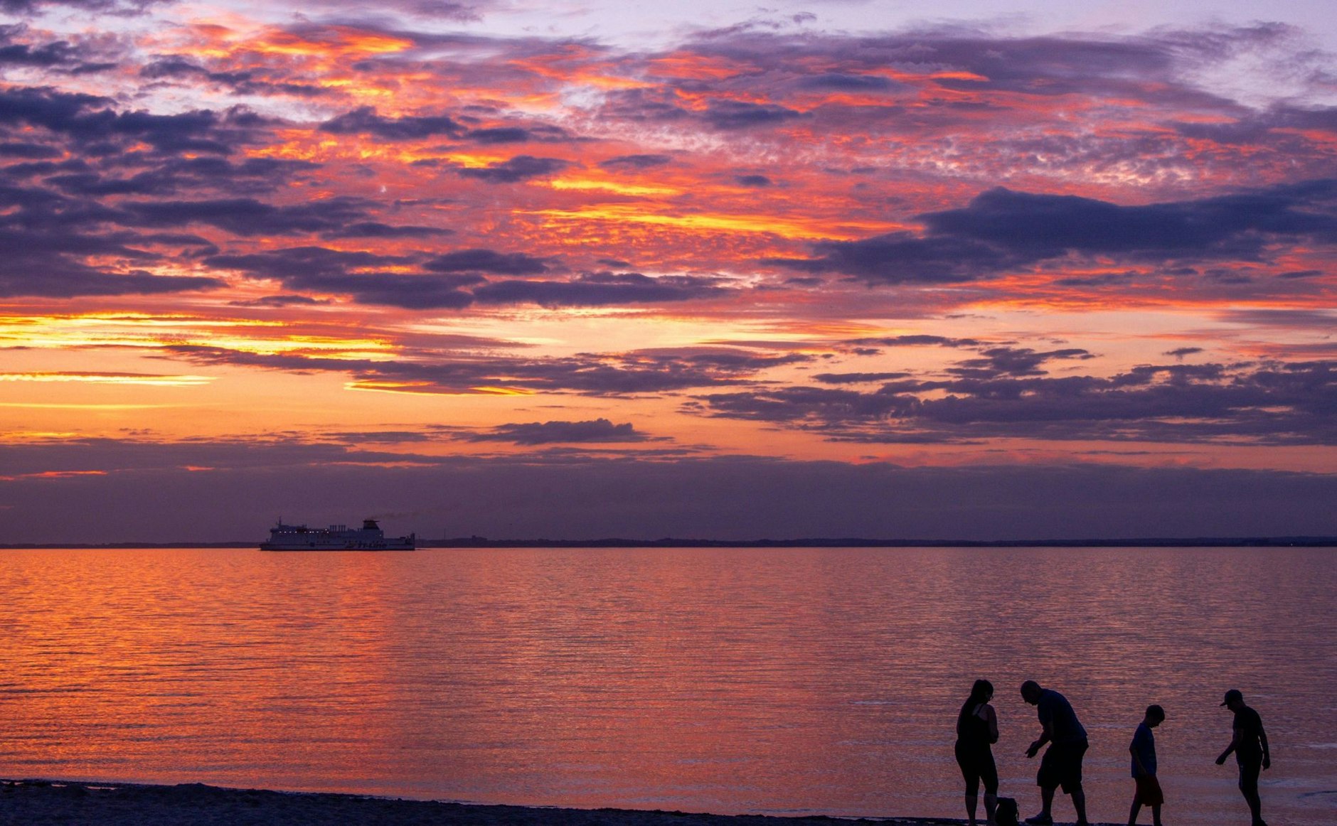 Eine Familie sammelt Steine während das schwedische Fährschiff "Huckleberry Finn" bei Sonnenuntergang über die Ostsee zum Hafen von Travemünde fährt.  