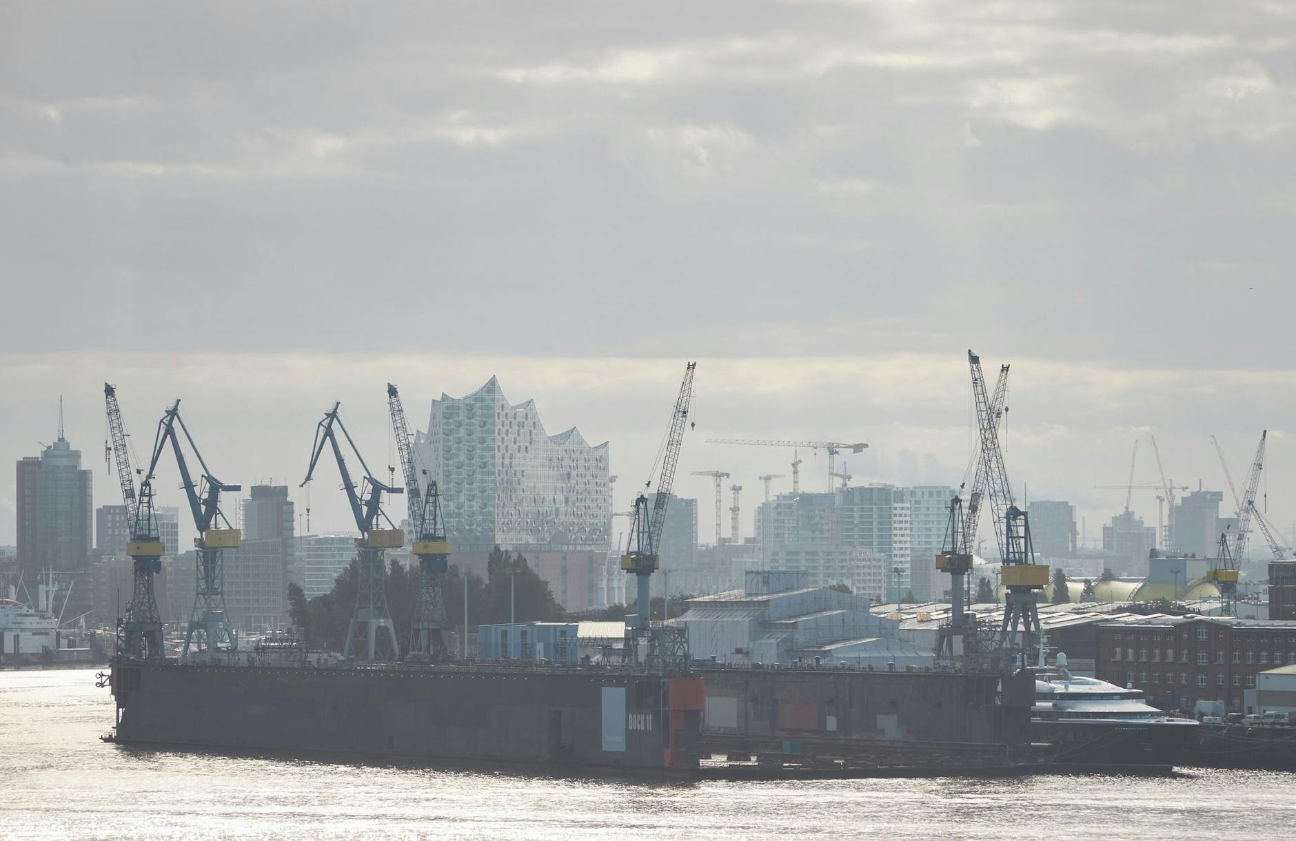 Die Elbphilharmonie ist hinter Kränen im Hamburger Hafen im Morgendunst zu sehen.
