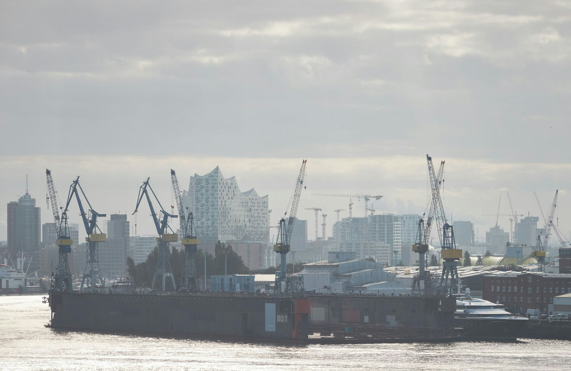 Die Elbphilharmonie ist hinter Kränen im Hamburger Hafen im Morgendunst zu sehen.  