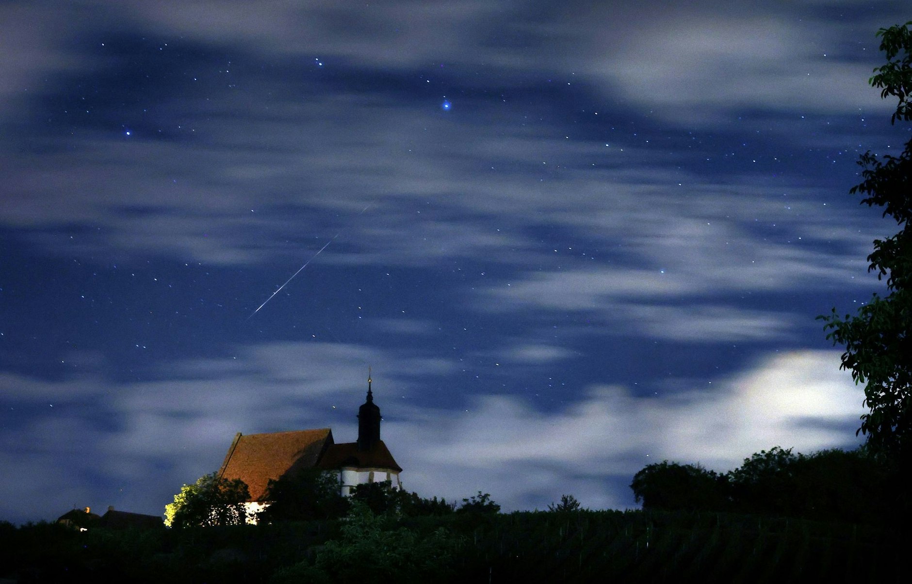 Eine Sternschnuppe verglüht am Himmel über der Wallfahrtskirche Maria im Weingarten in Bayern. Der Sternschnuppenstrom der Perseiden erreicht am Wochenende seinen Höhepunkt.  