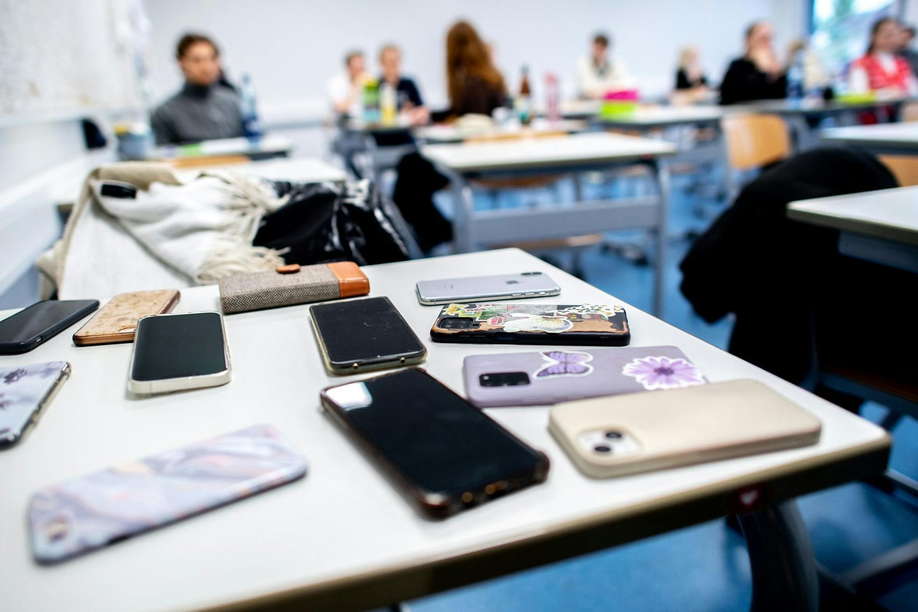 ARCHIV - Zahlreiche Smartphones der Schülerinnen und Schüler liegen vor Beginn einer Abiturprüfung auf einem Tisch im Klassenzimmer.
