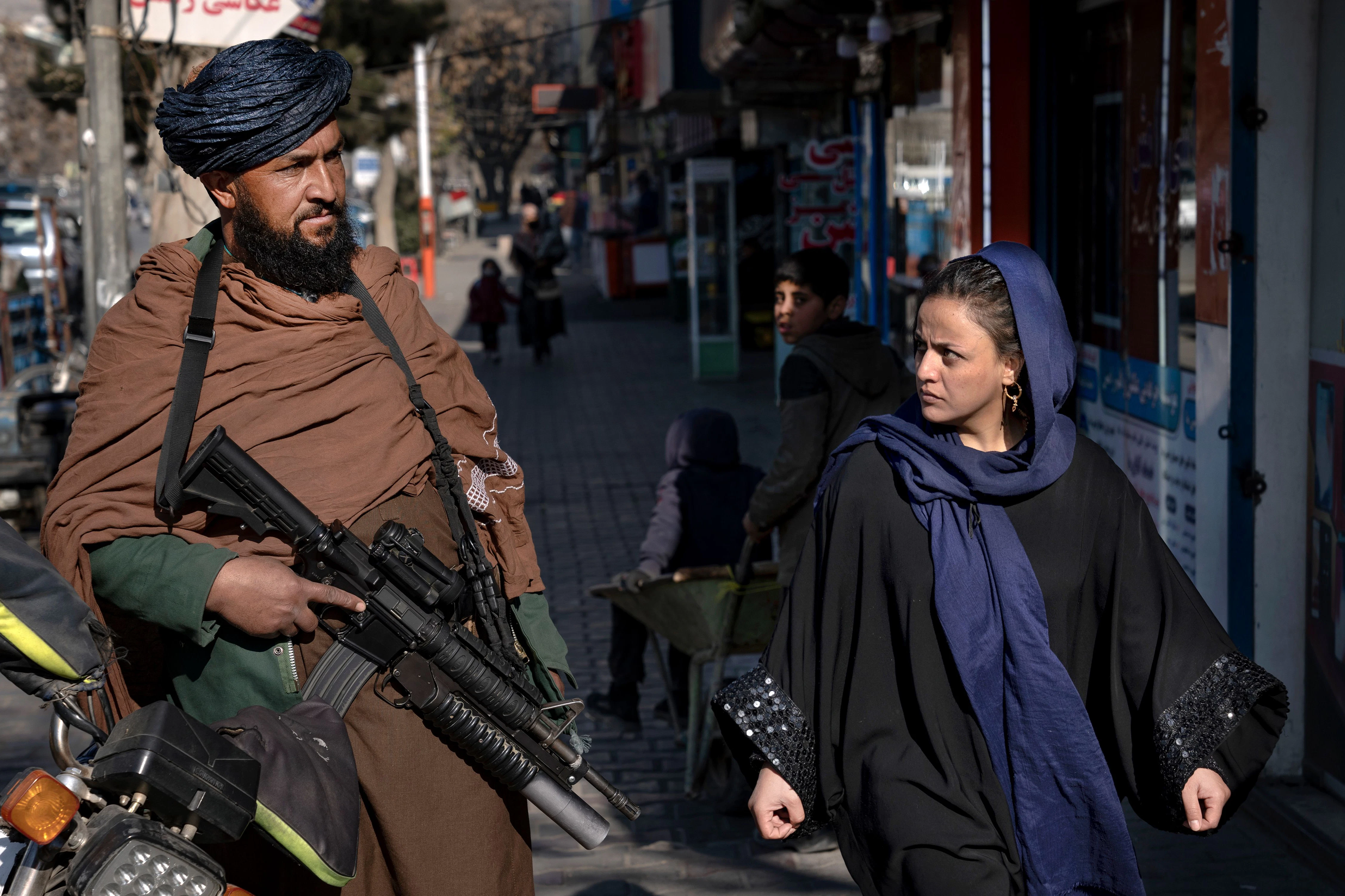 Ein Taliban-Kämpfer steht Wache, während eine Frau vorbeiläuft.