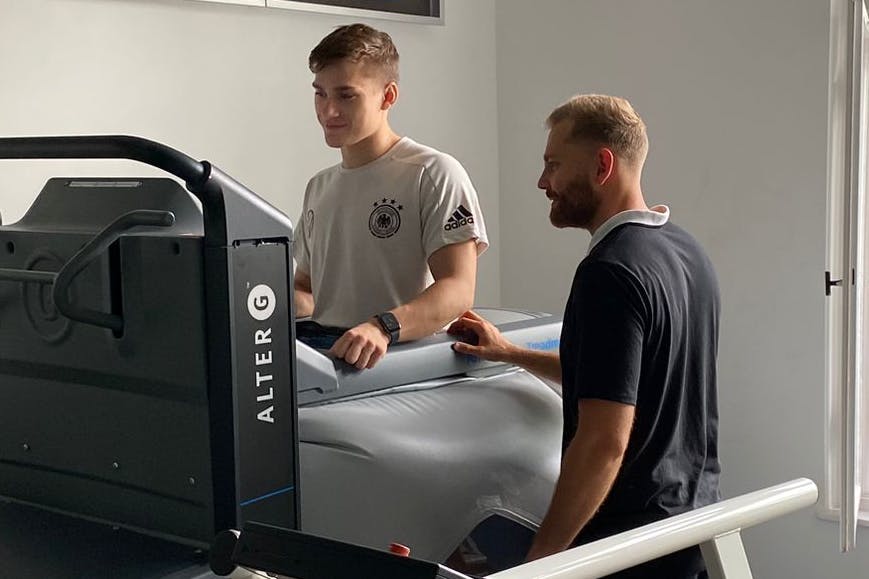 Physiotherapeut Nils Vielrose vom Bewegungswerk Berlin erklärt BFC-Verteidiger John Liebelt (l.), wie das Hightech-Laufband funktioniert.