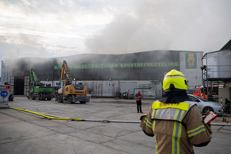 Kräfte der Berliner Feuerwehr sind an einer Halle eines Holz- und Baustoffrecyclingunternehmens im Einsatz.  
