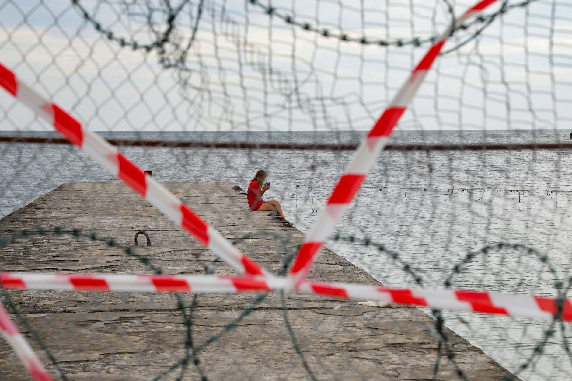 Hinter Stacheldraht und Absperrband genießen Urlauber die Zeit am Strand in Odessa.