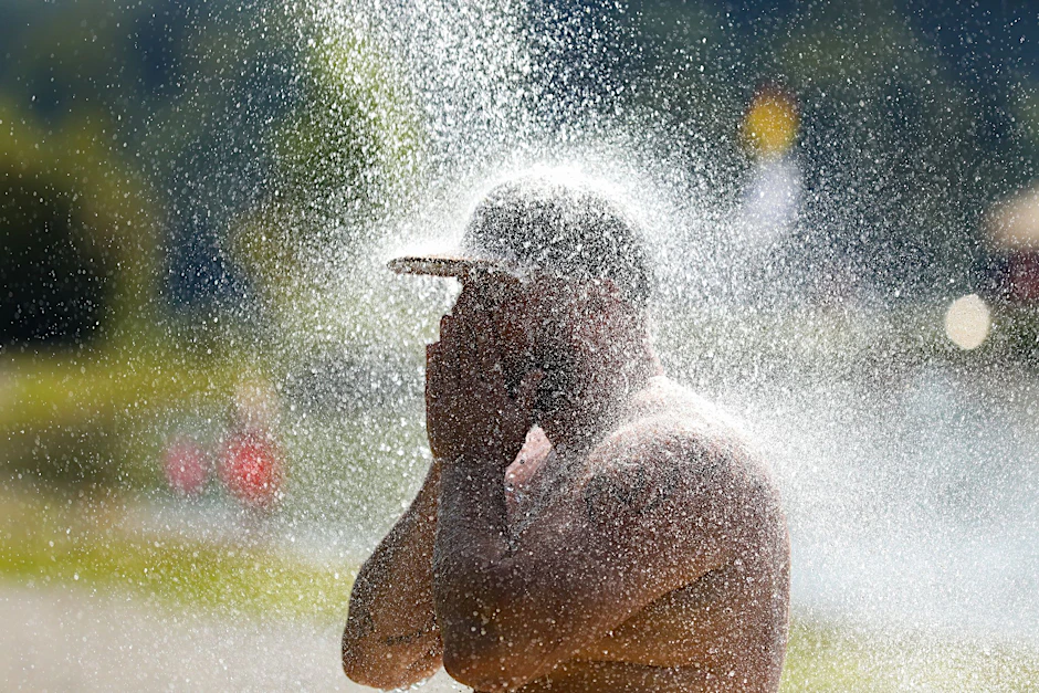 Ein Mann erfrischt sich an einem Badesee unter einer kalten Dusche.  