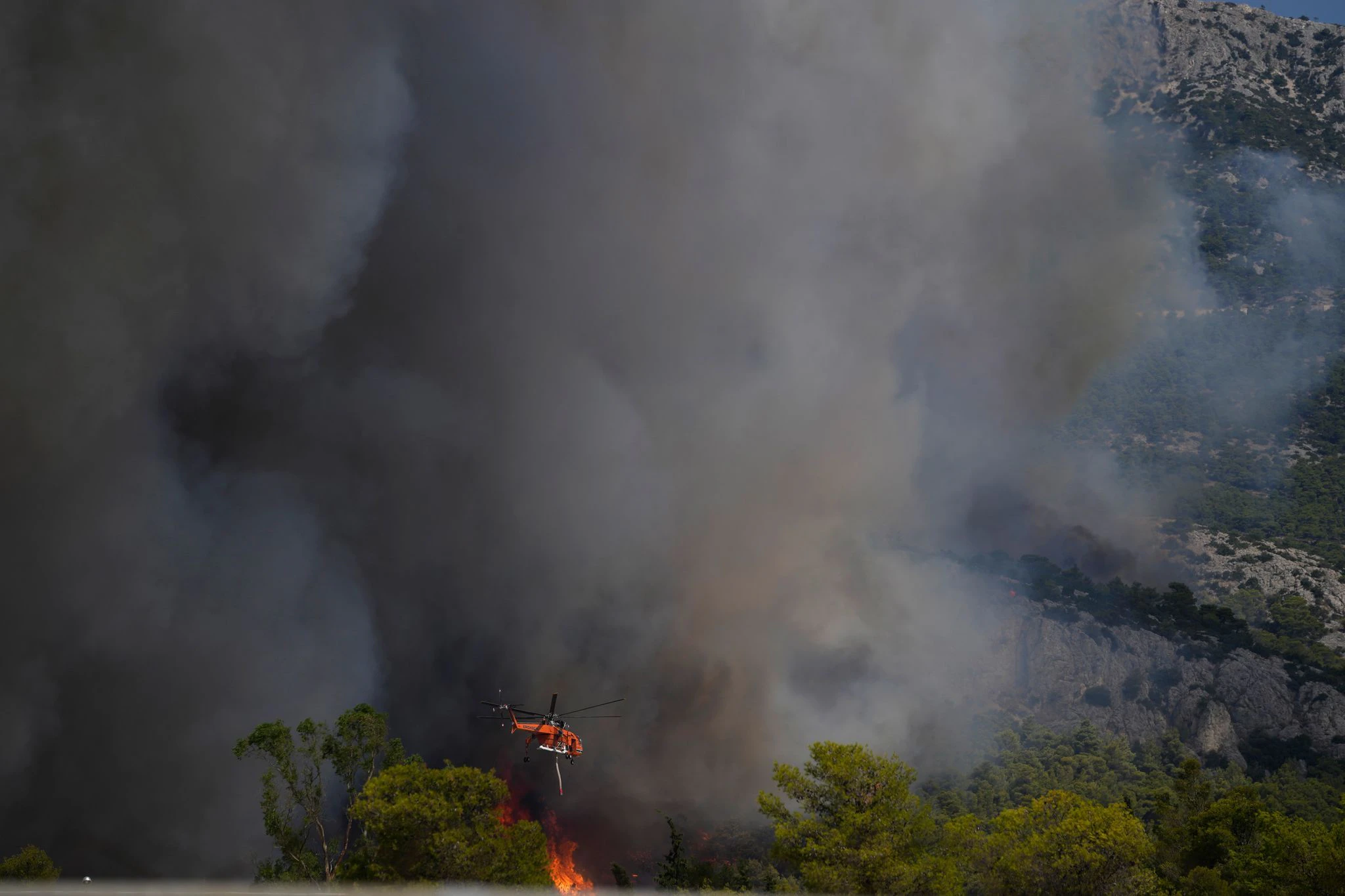 dpatopbilder - Ein Feuerwehrhubschrauber wirft Wasser auf die Flammen nahe des Militärstützpunkts Kapota im Gebirge Parnitha.  