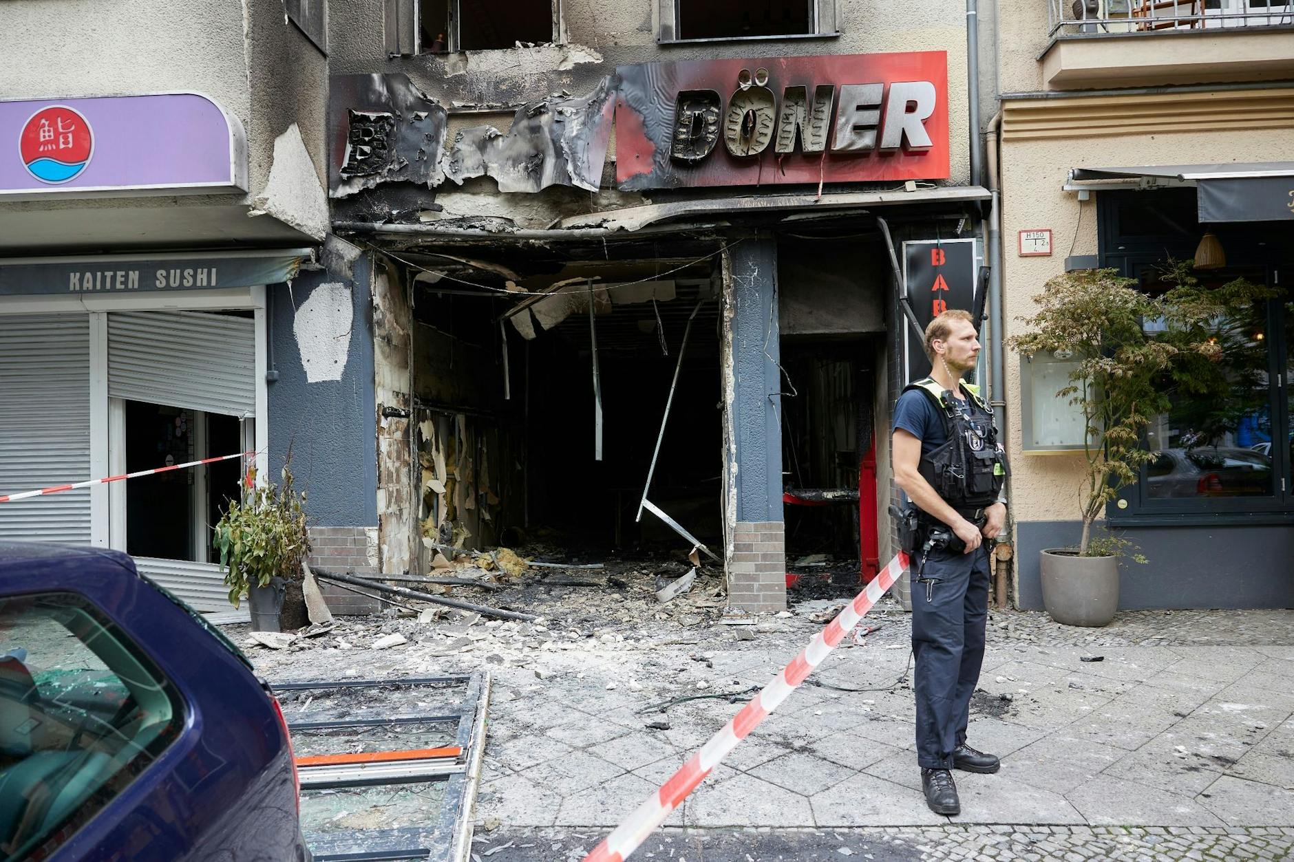 Ein Polizist steht vor einem ausgebrannten Dönerimbiss in der Uhlandstraße.