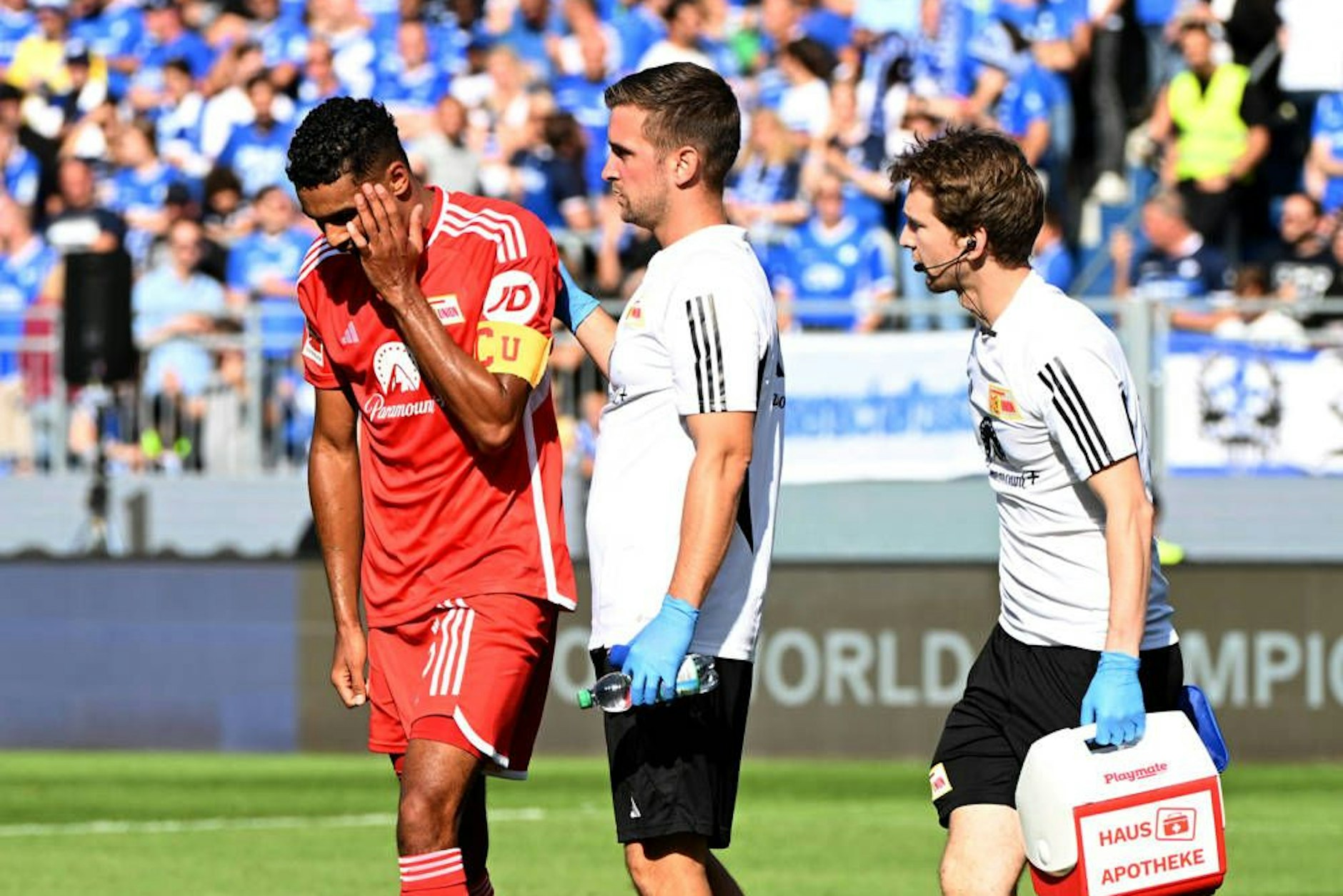 Danilho Doekhi wird von Mannschaftsarzt Marvin Minkus (M.) und Physiotherapeut Maximilian Perschk vom Platz begleitet. Der Niederländer spielt aber trotz Jochbeinbruch weiter.