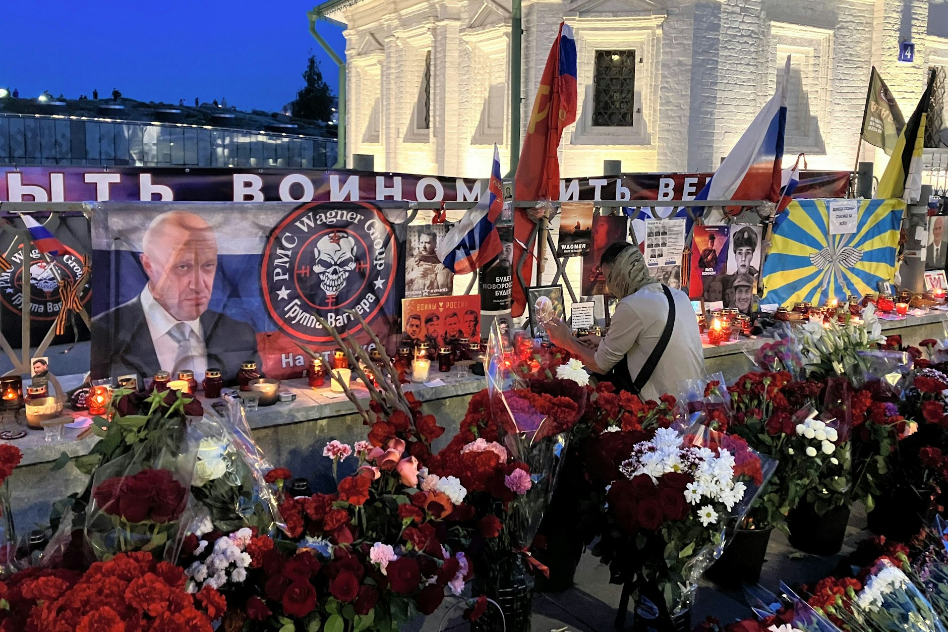 Ein Mann legt einen Gegenstand zwischen Blumen und Kerzen an die Gedenkstätte für den toten Söldnerchef Prigoschin im Zentrum von Moskau.