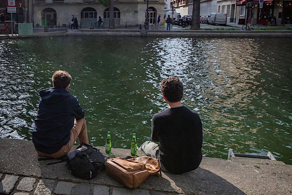 ARCHIV - Zwei junge Männer trinken am Ufer des Kanals Saint-Martin in Paris gemeinsam Bier.  