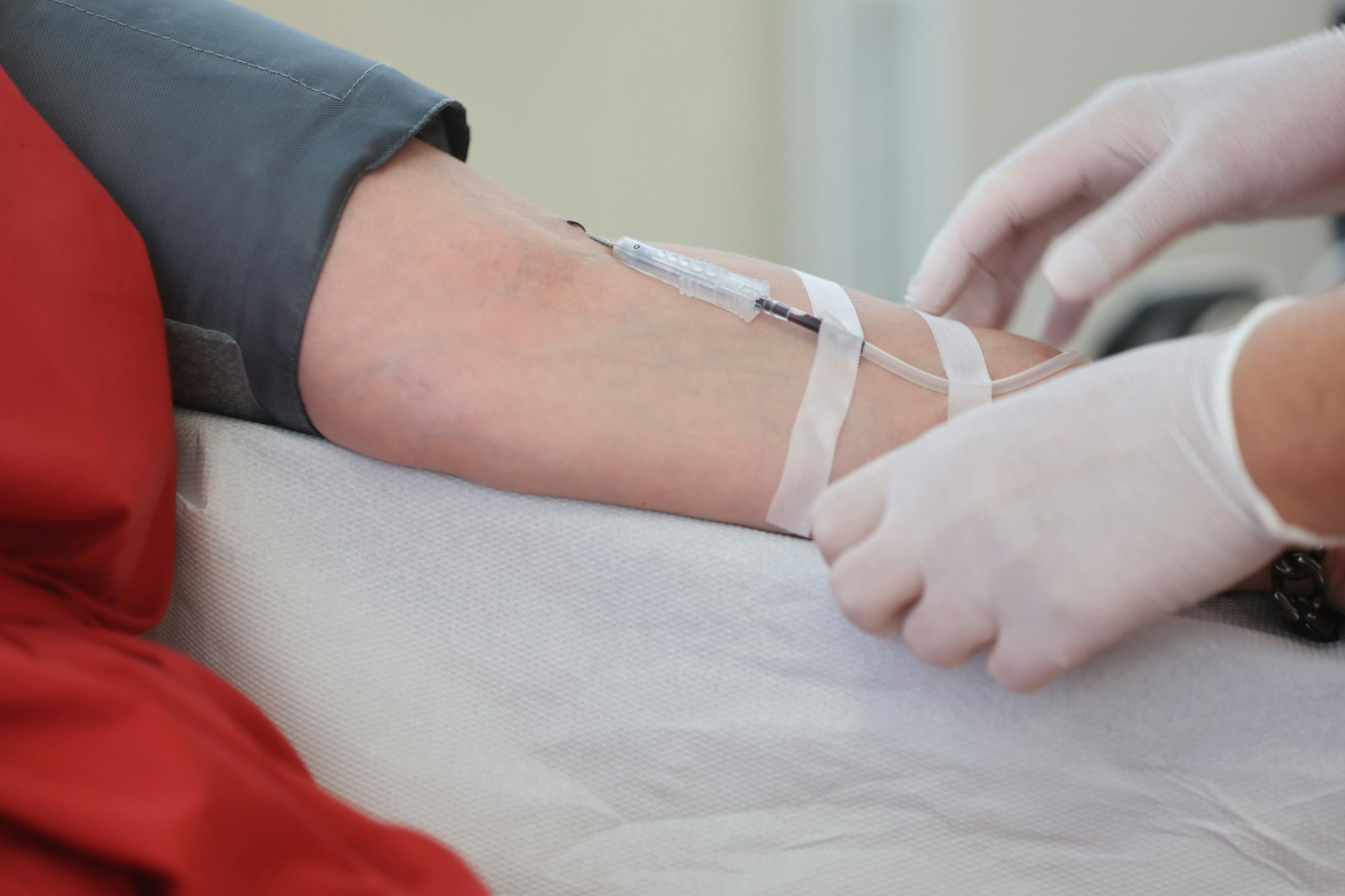 Eine Venenkanüle ist bei einer Blutspende am Arm eines Spenders fixiert.