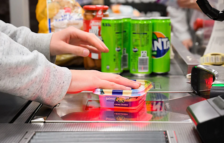 Eine Kassiererin scannt Lebensmittel an der Kasse eines Supermarktes.  