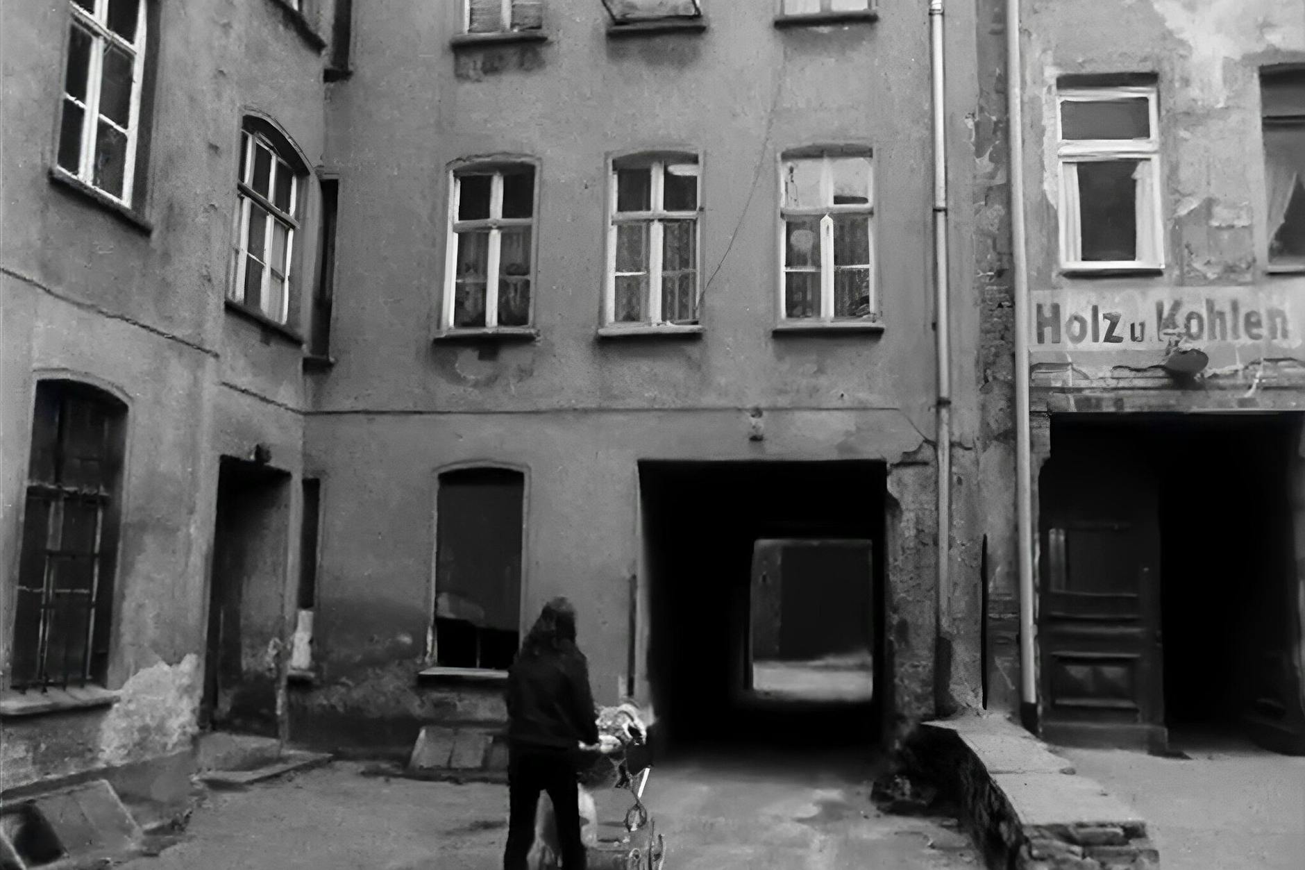 Szenenfoto aus dem SFD-Filmmaterial zum Thema Wohnungsprobleme. Eine junge Frau schiebt einen Kinderwagen über einen Hinterhof in Ostberlin. 