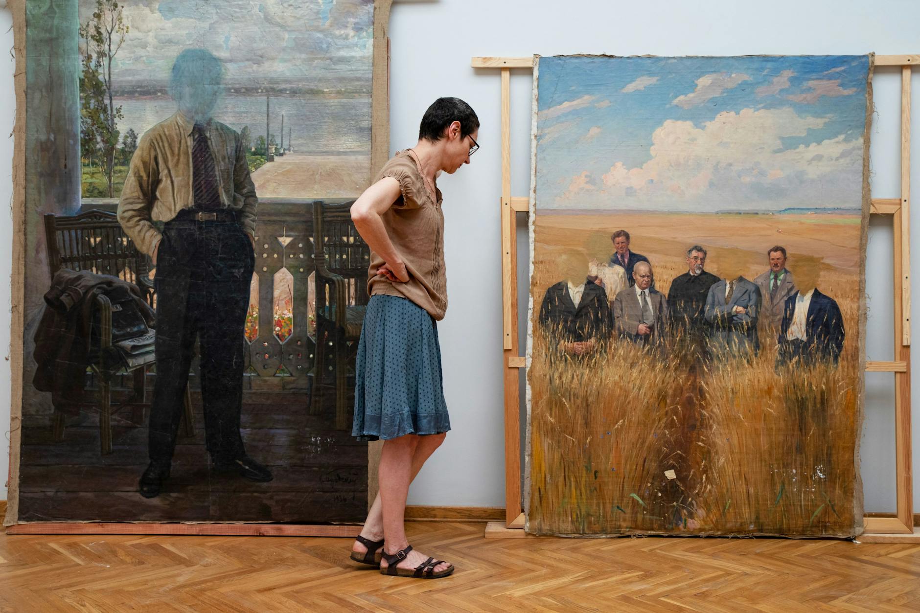 Nadia Kaabi-Linke vor Bildern aus der Spetsfond-Sammlung. Die in Ungnade gefallenen Protagonisten wurden von Zensoren von den Bildern gewaschen. Links ein Porträt des Künstlers Isaak Brodskis von unbekannter Hand und unbekannten Datums, rechts das Werk „Erntebesichtigung“ von Jefim Tschepzow (1937)