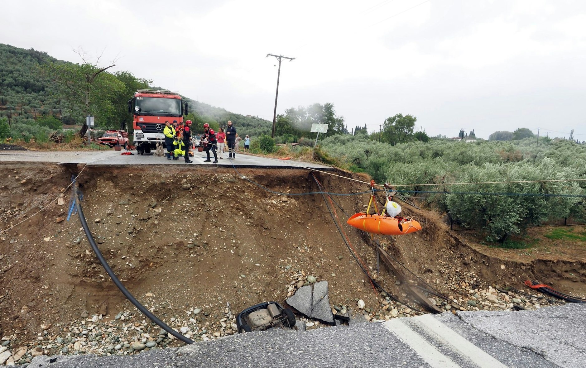 Feuerwehrleute verwenden Seile, um einen Nierenpatienten auf einer Trage über eine durch einen Regensturm beschädigte Straße zu transportieren.  
