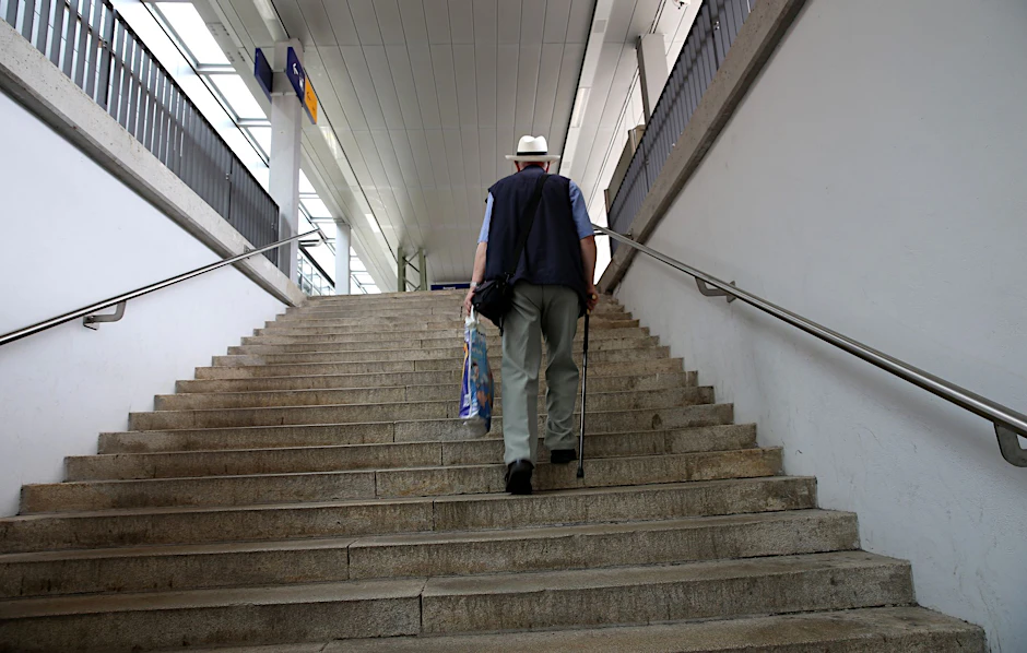 Ein älterer Mann mit Gehstock geht auf einer Treppe in einer Bahnhofsunterführung.&nbsp;