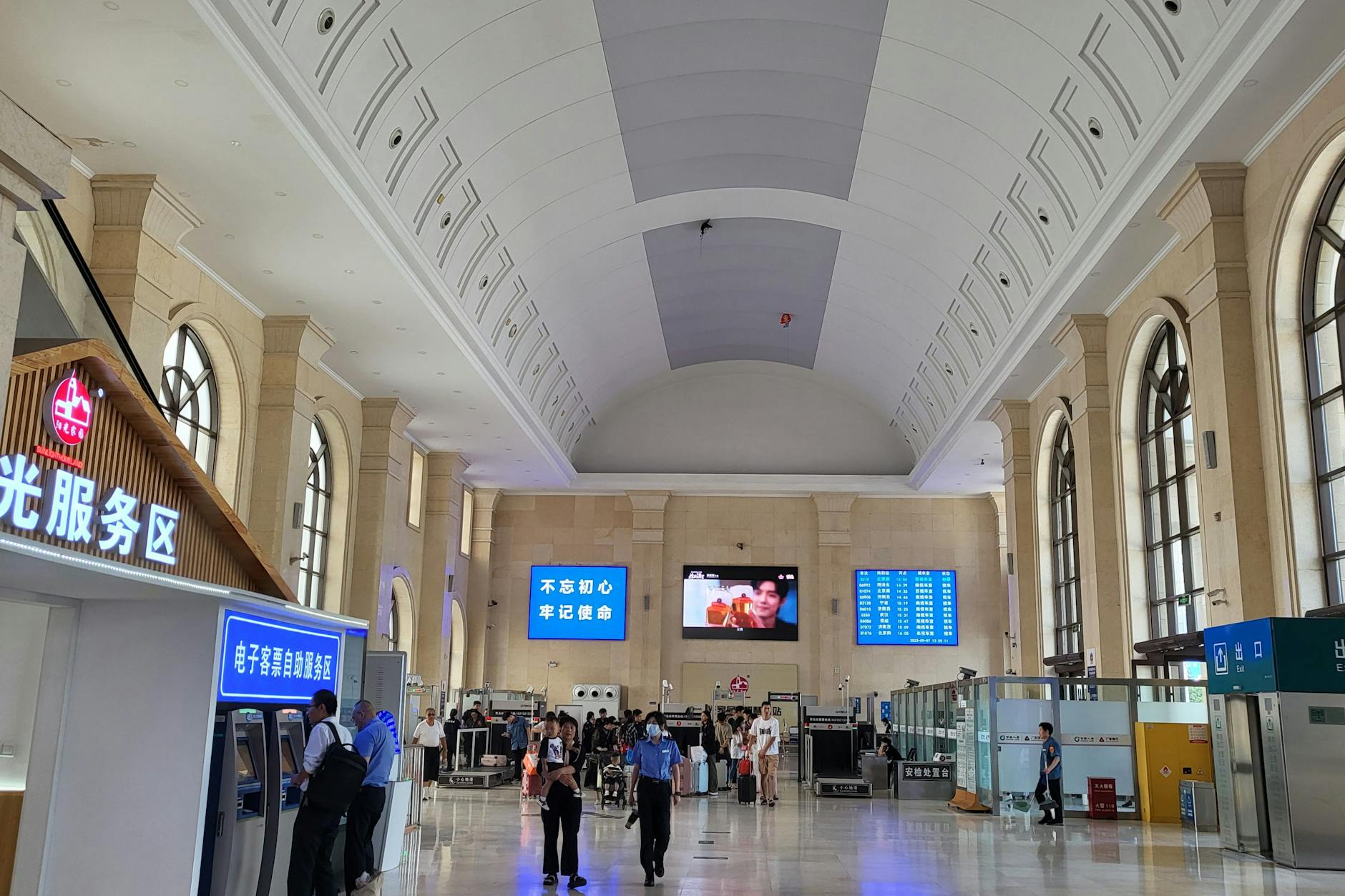 Blick in die Bahnhofshalle mit Tonnengewölbe in Qingdao aus der Zeit von Kaiser Wilhelm II.: Passagiere gehen durch eine Sicherheitskontrolle, bevor sie in die Wartehallen gelangen. Der Betrieb ist durchdigitalisiert.