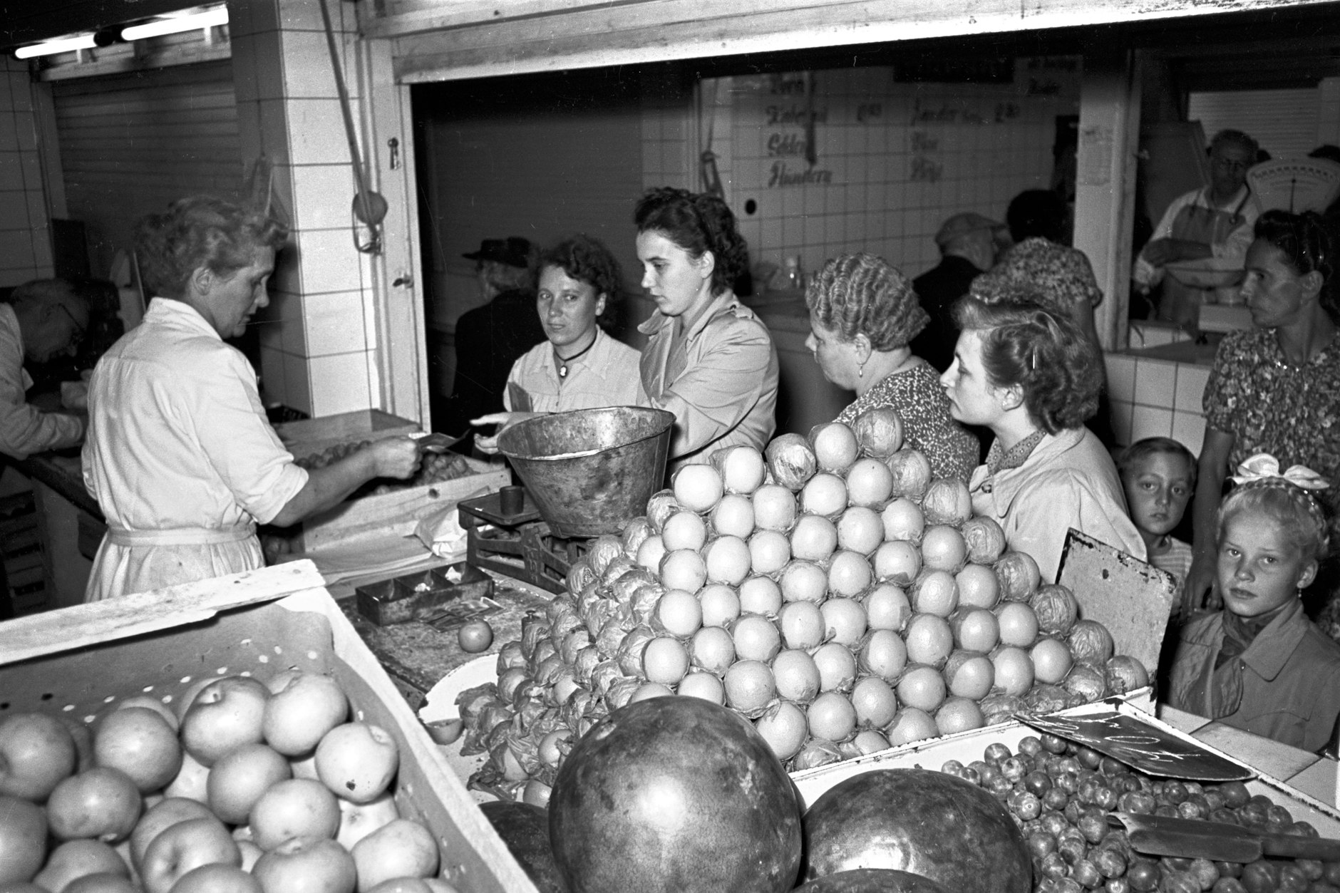 Obststand mit Äpfeln, Apfelsinen und Melonen in der Zentralmarkthalle am Alexanderplatz in Berlin, aufgenommen um 1958. Die aus Ägypten importierten Orangen waren beliebt, die aus Kuba nicht.