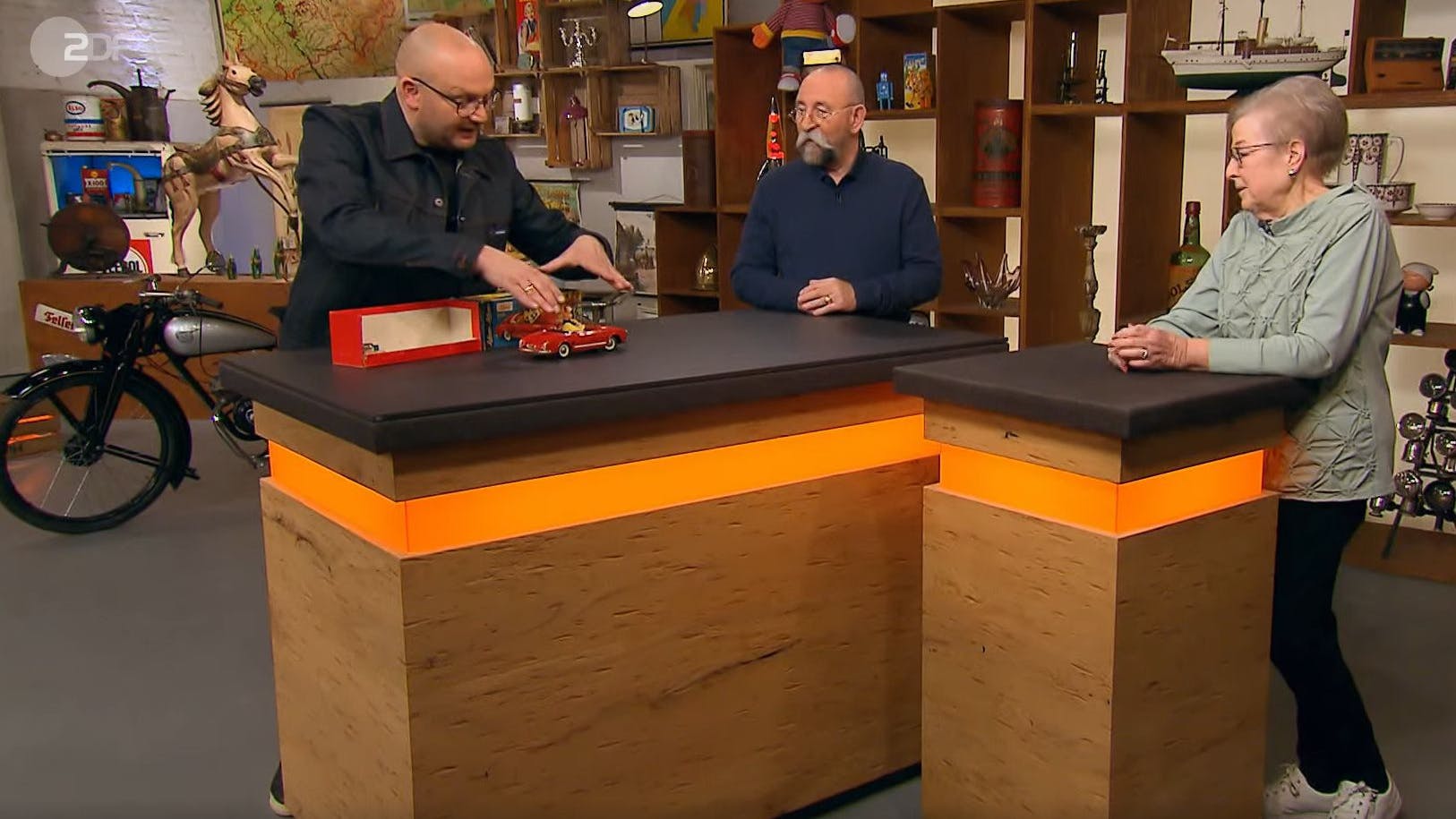 Am „Bares für Rares“-Expertentisch war die Welt noch in Ordnung. Drei Menschen sind von dem Alfa Romeo begeistert.