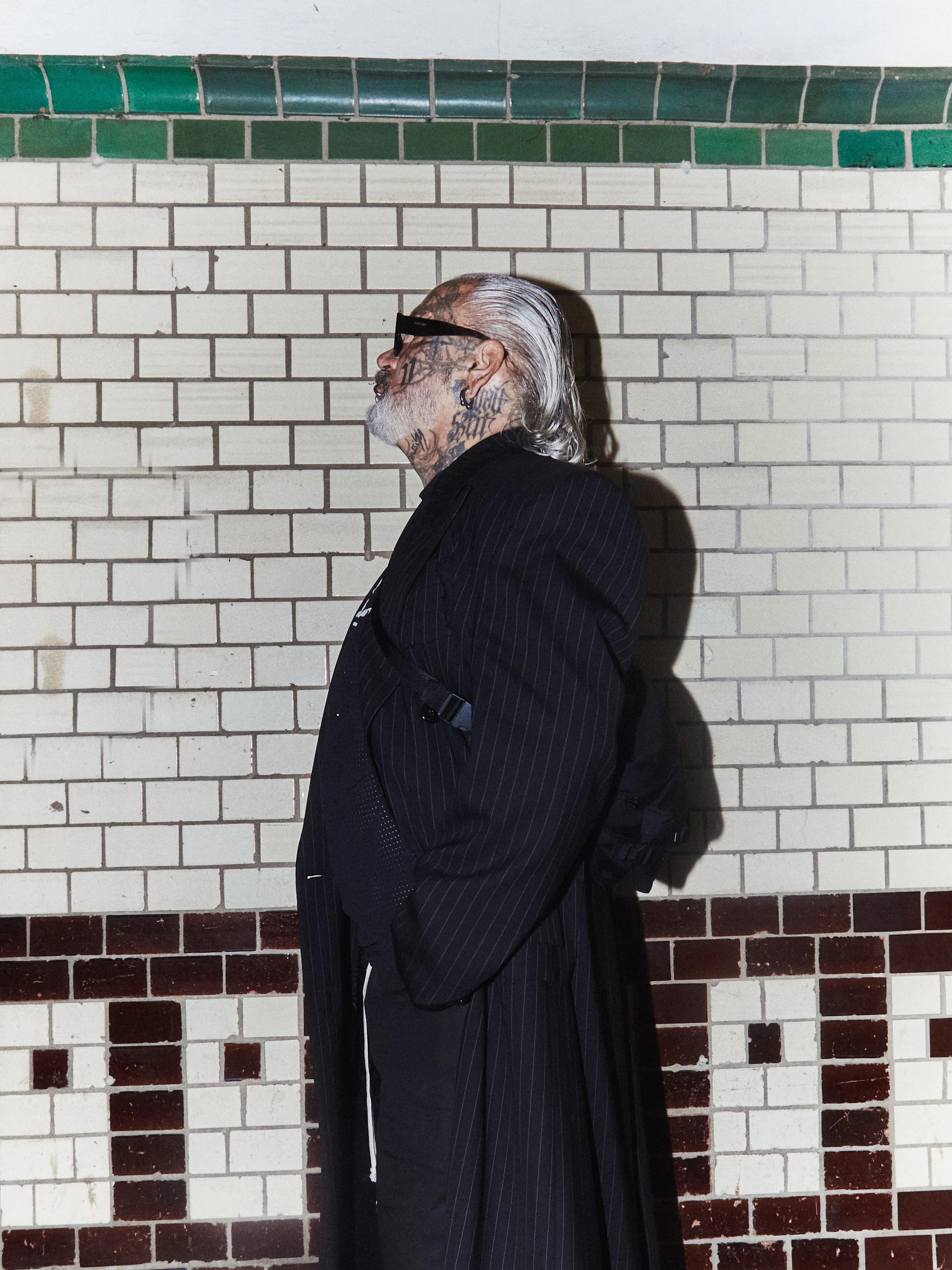 Unverkennbar Marquardt: Wet Look und Sonnenbrille (von Prada). Dazu trägt der Berliner Fotograf einen Nadelstreifenmantel von Vetements und Cowboystiefel von Dries Van Noten. Top und Shorts: Rick Owens x Champion.