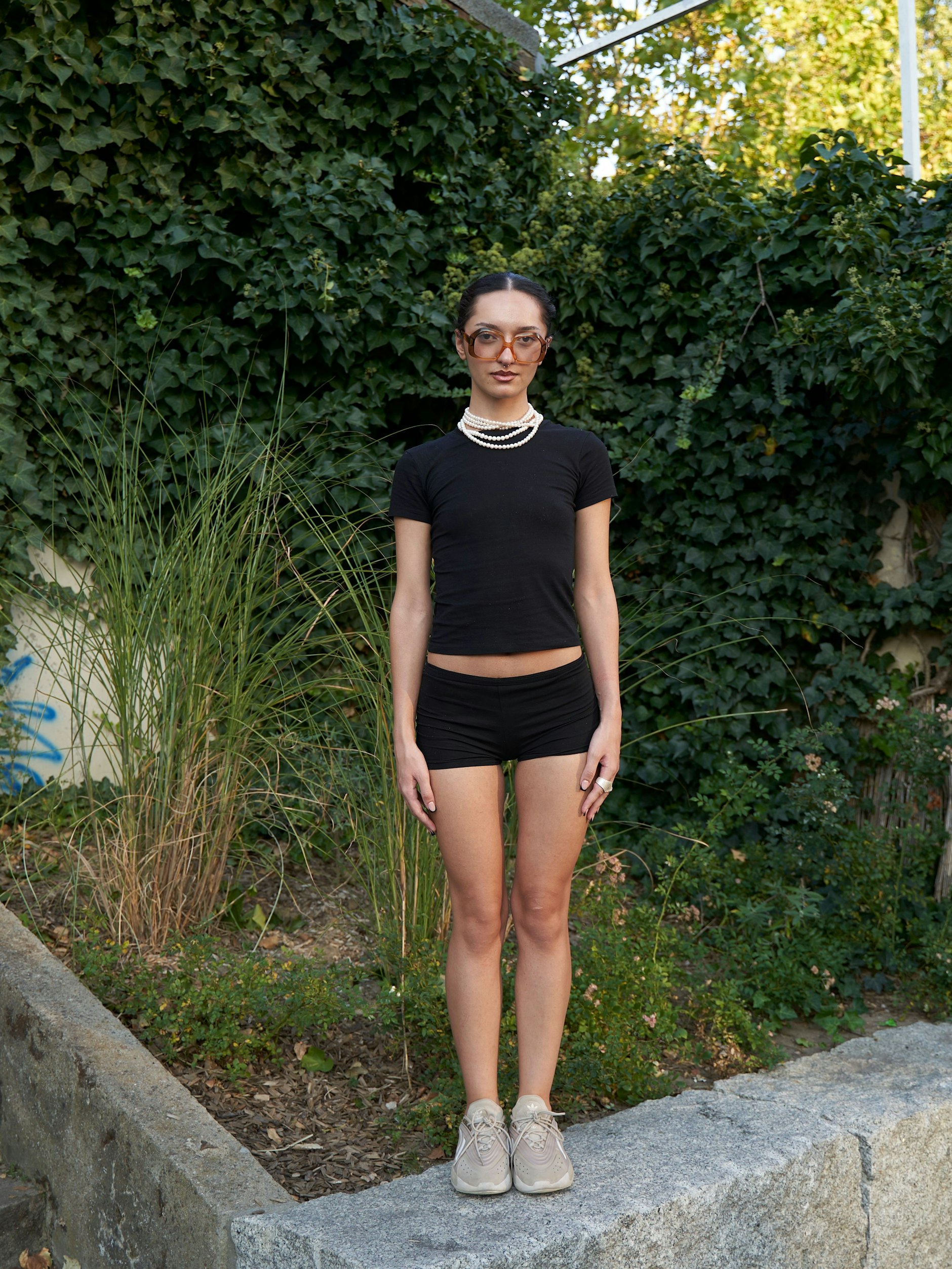 Simay zeigt uns, was Accessoires bewirken können. Der super simple, schwarze Look aus engem T-Shirt und knappem Höschen wird durch die mehrfach um den Hals gewickelte helle Perlenkette und die riesengroße Vintagebrille zum Hingucker. Dazu kombiniert Simay ein Paar Adidas Ozelia in elegantem Greige. Simay ist zu Besuch in Berlin, sie studiert Kunstgeschichte in Eskişehir (Türkei).