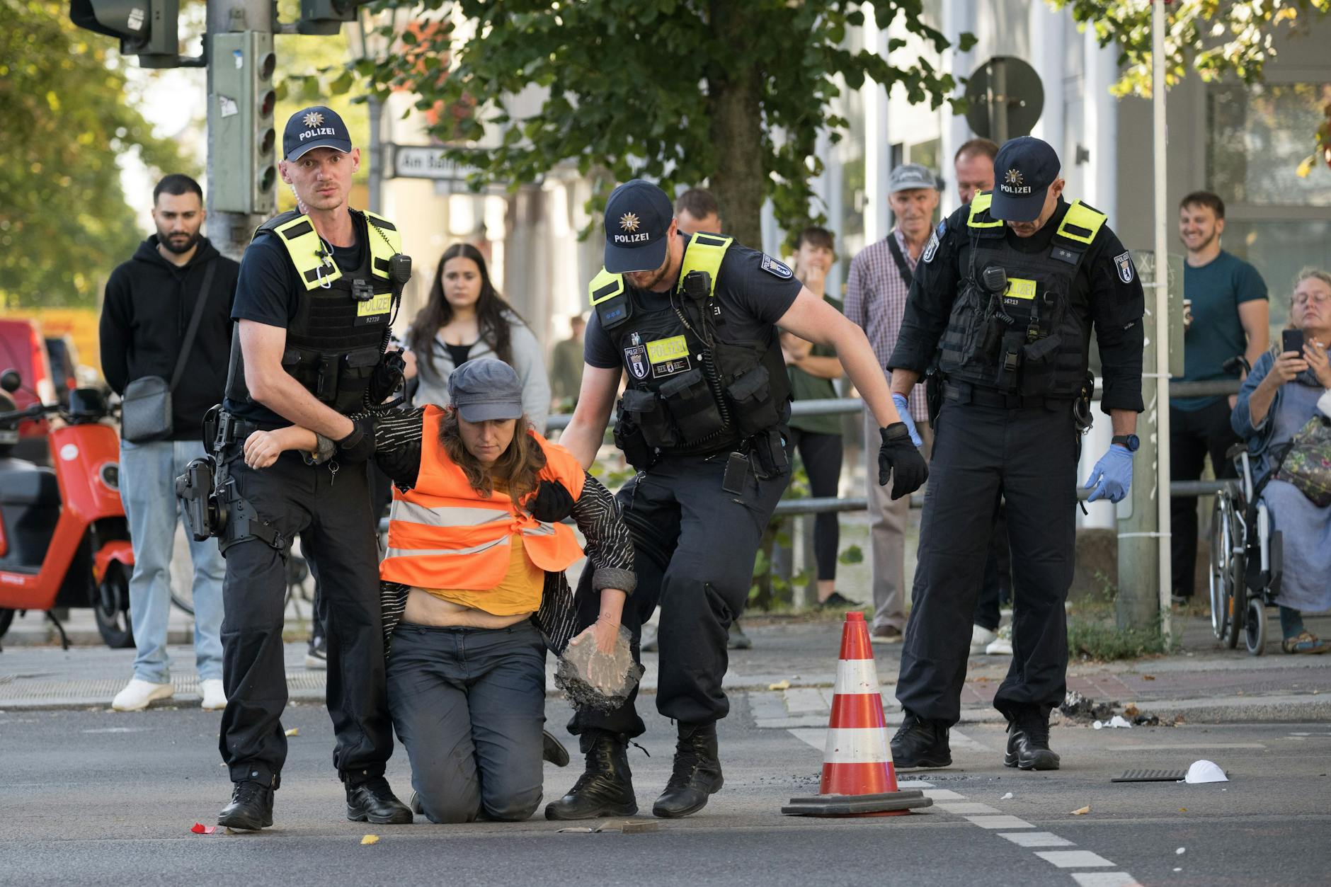 Eine Aktivisten der Klimaschutzgruppe Letzte Generation wird von Polizeibeamten am Spandauer Damm über die Straße getragen, nachdem sie mit schwerem Gerät befreit werden musste.