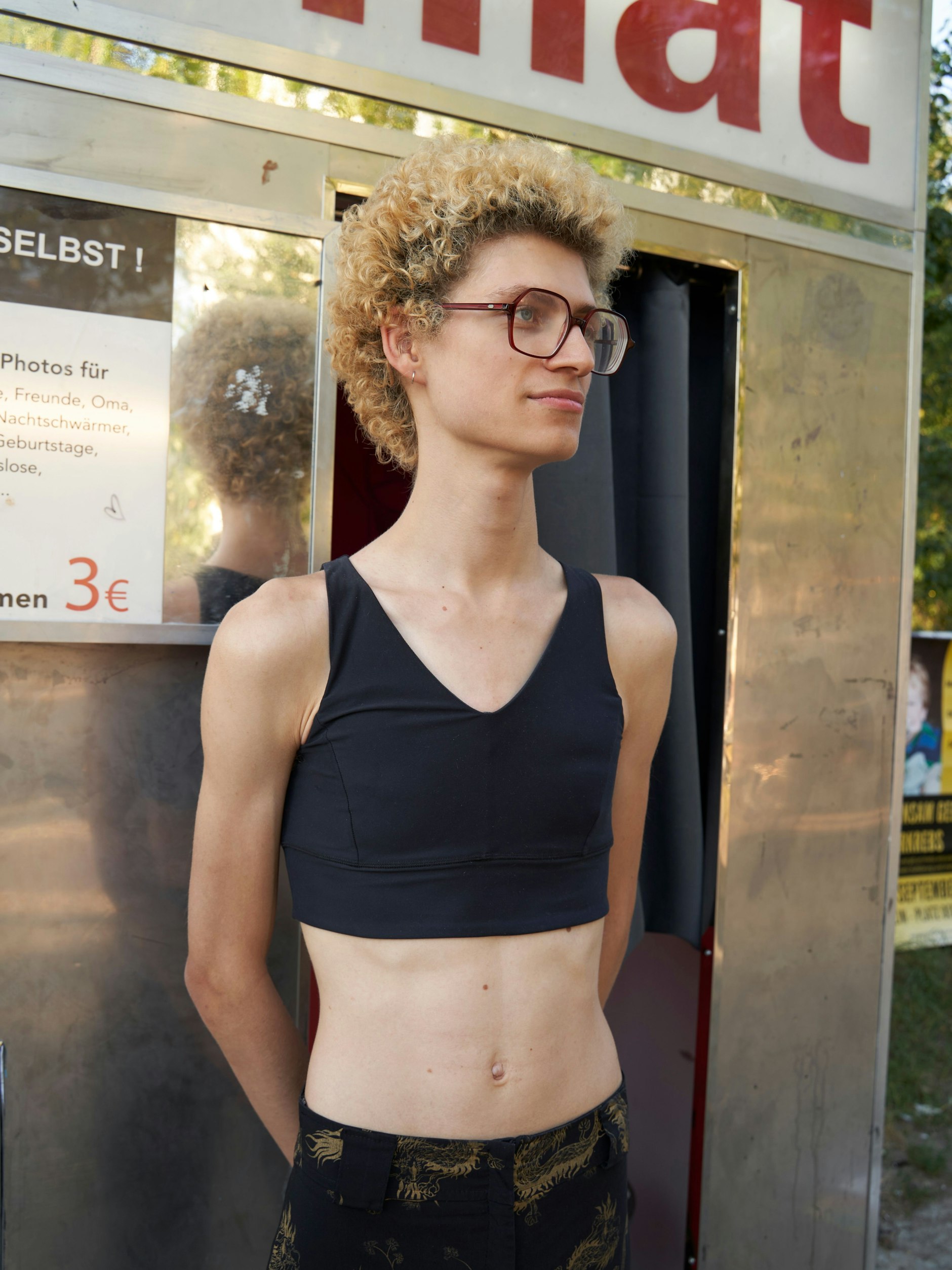 Alexandre lebte in Paris, bevor er nach Berlin zog, um die Studiengänge Mathematik, Computerwissenschaft und Musikalische Improvisation zu belegen. Bei dieser spannenden Kombination ahnt man seinen Berufswunsch: Er will Forscher werden. Ein feminin geschnittenes Sportoberteil hat er zum bauchfreien Sommertop umfunktioniert, die Hose ist Secondhand. Die weißen Stoffschuhe hat er bei Muji gekauft. Die Brille ist aus Paris; auch wenn sie wie ein Fashion-Accessoire aussieht, sie hat <a href="https://www.google.com/search?sca_esv=566970484&amp;rlz=1C5CHFA_enDE914DE914&amp;q=Dioptrien&amp;spell=1&amp;sa=X&amp;ved=2ahUKEwjl6LKg1bmBAxUIxQIHHfzaASsQkeECKAB6BAgLEAE">Dioptrien</a>! Alexandres Locken seien echt, und er müsse manchmal ganz schön mit ihnen kämpfen, sagt der angehende Wissenschaftler.