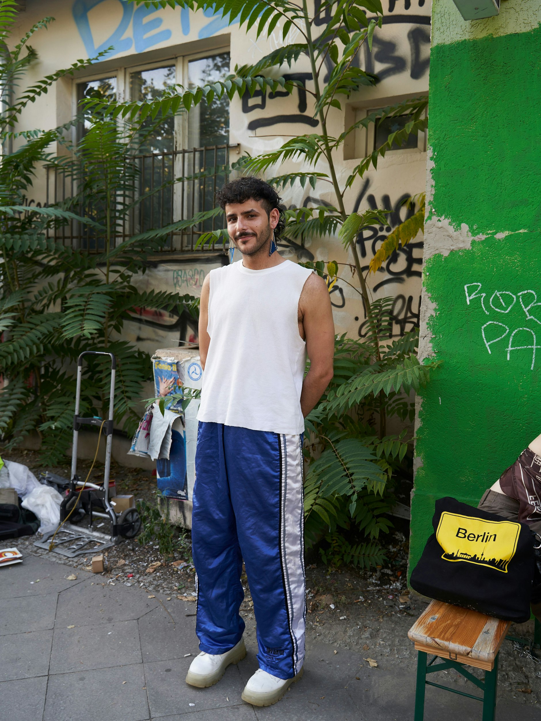 Mo studiert Mode mit dem Schwerpunkt Marken und Kommunikation in Amsterdam. Derzeit wohnt er in Berlin, weil er ein Praktikum bei einem Berliner Label macht. „Ich finde fast alle meine Sachen auf der Straße“, sagt Mo. Das trifft, bis auf die Buffalo-Schuhe aus veganem Leder, auch auf sein heutiges Outfit zu: Sporthosen und Top, von dem Mo die Ärmel abgeschnitten hat. Was die Berliner so alles vor die Tür stellen!