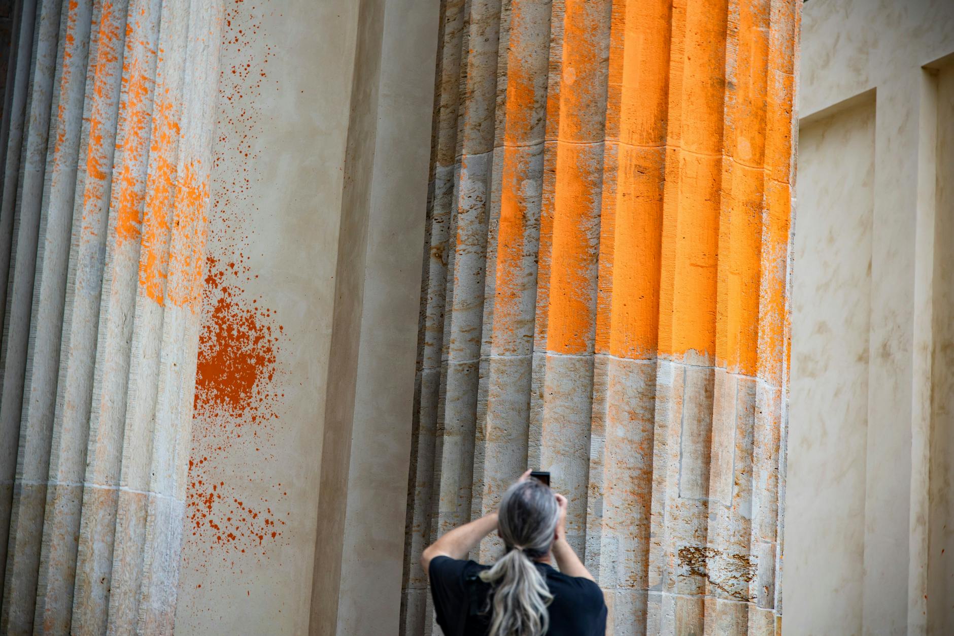 Eine junge Frau fotografiert die orange-gefärbte Säule aus der Nähe.