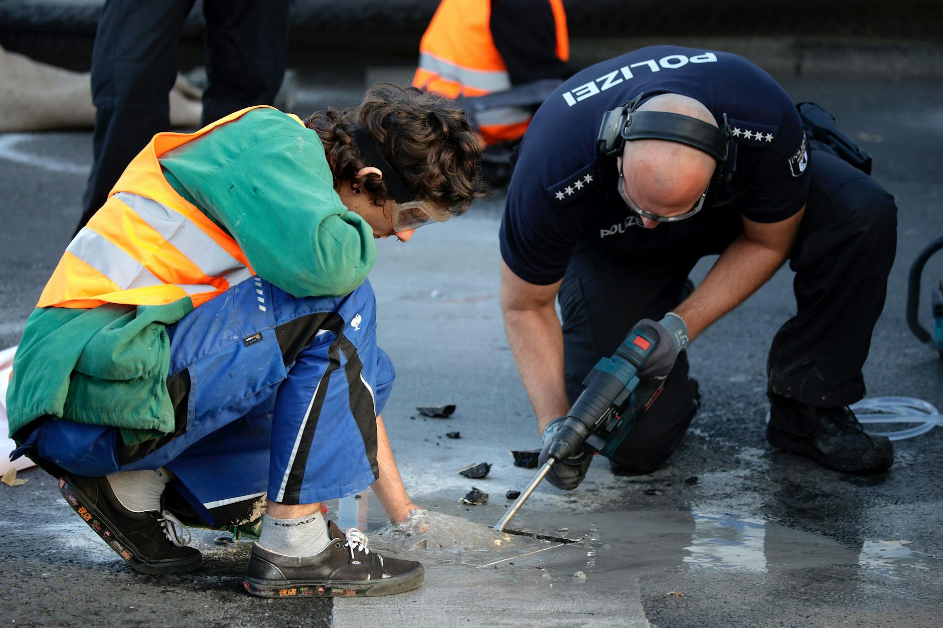 Berlin: Ein Polizist entfernt mit einem Bohrer einen Teil Asphalt, um einen Aktivisten von der Straße zu lösen. Am Dienstag fanden erneuet Protestaktionen der Klima-Aktivisten der Letzten Generation statt.