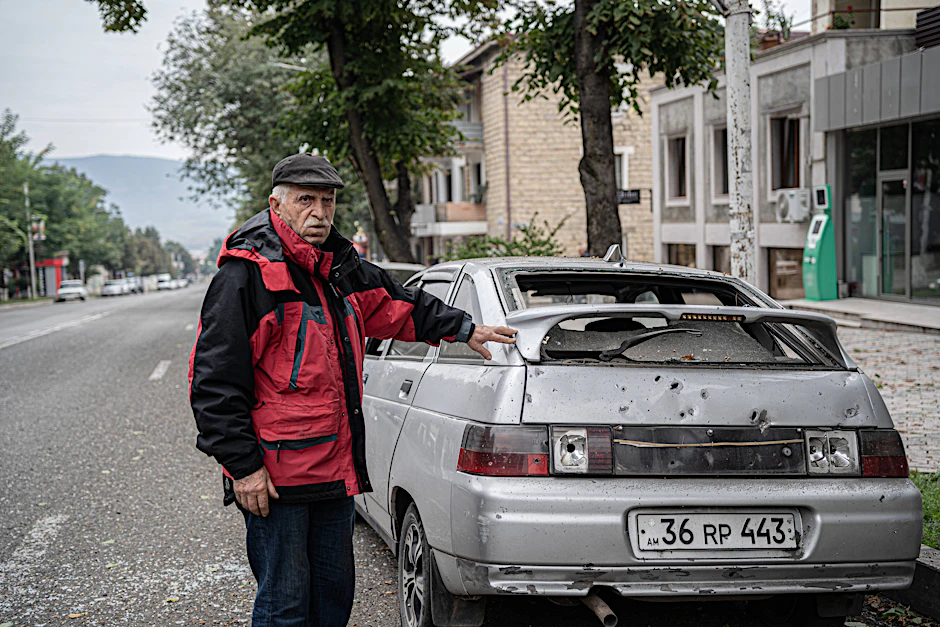 Ein Mann steht neben einem durch Granatenbeschuss beschädigten Auto in Stepanakert.