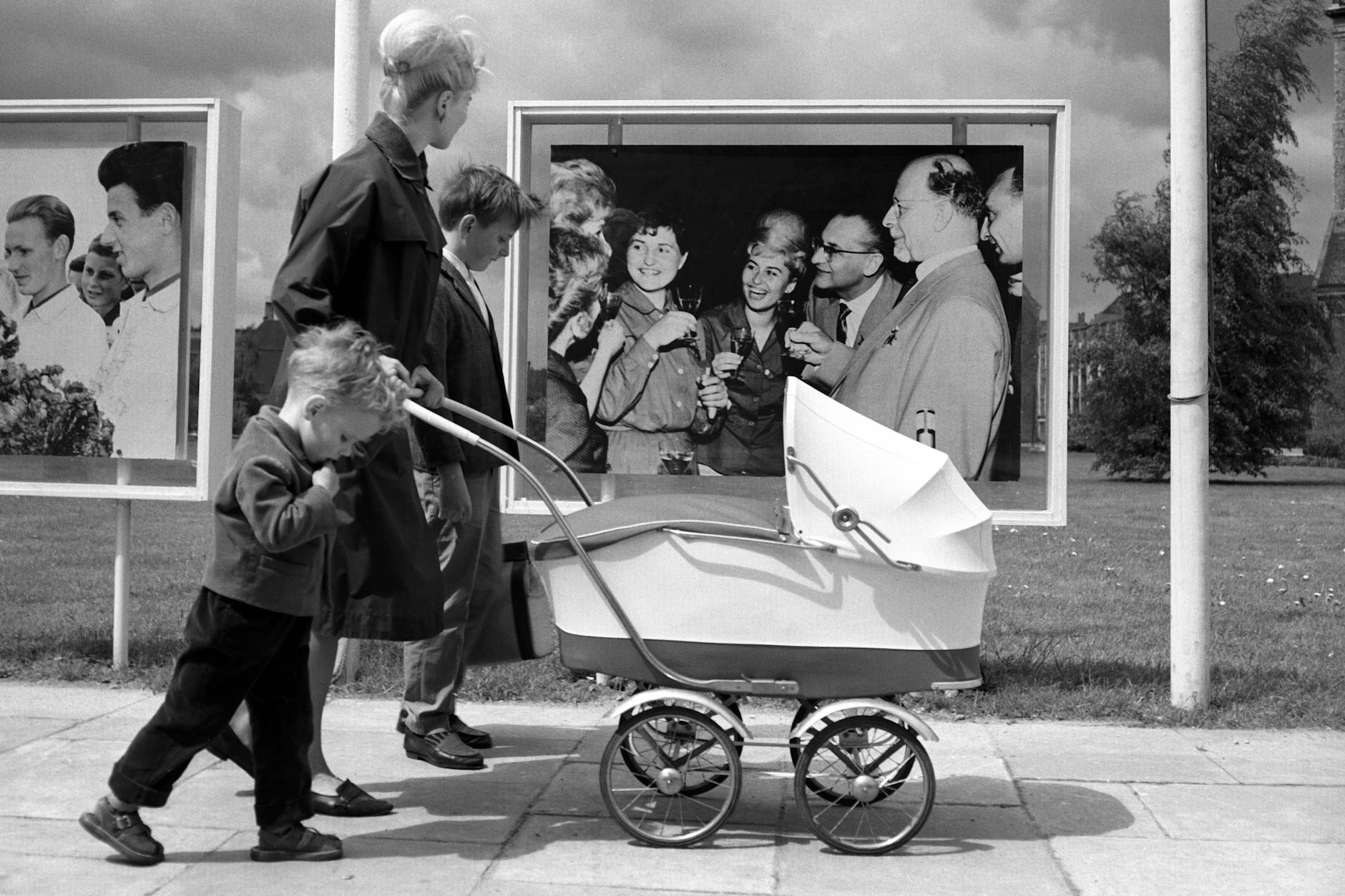 Eine junge Mutter mit Kinderwagen und ihren Kindern vor einem Propagandafoto Ulbrichts in Ost-Berlin