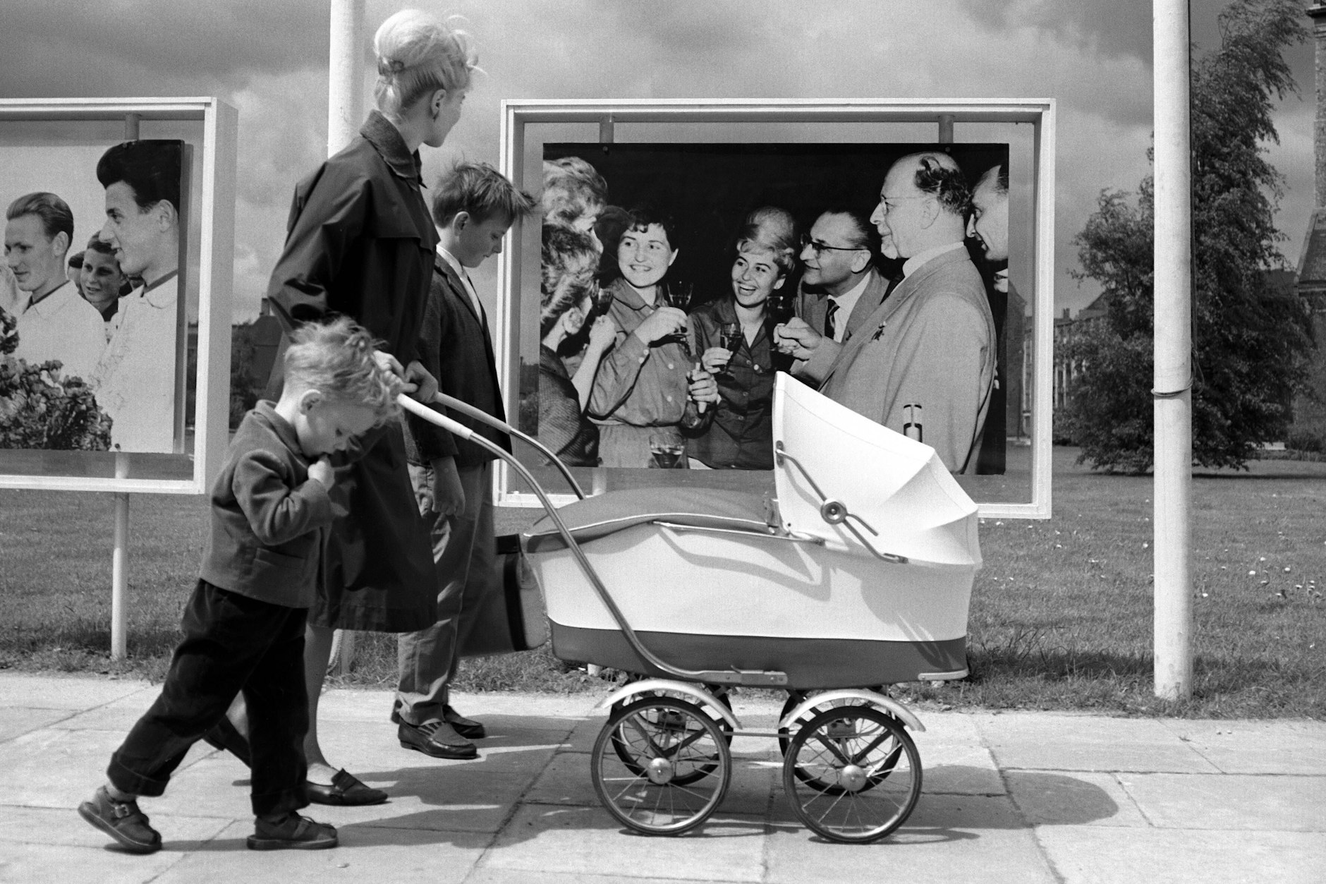 Eine junge Mutter mit Kinderwagen und ihren Kindern vor einem Propagandafoto Ulbrichts in Ost-Berlin