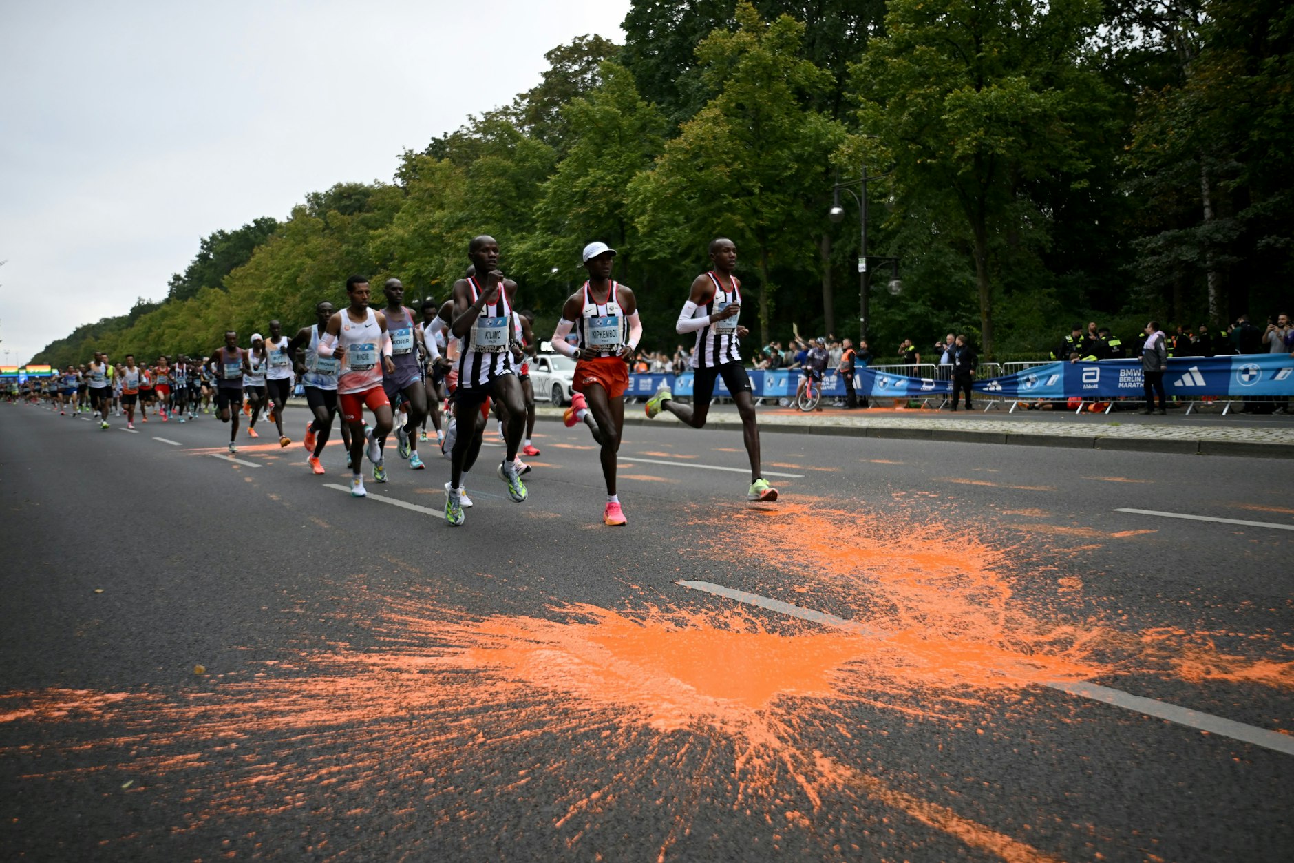 Teilnehmer des Marathons laufen durch die orangefarbene Farbe, die von Aktivisten der "Letzten Generation" auf den Asphalt geschüttet wurde.