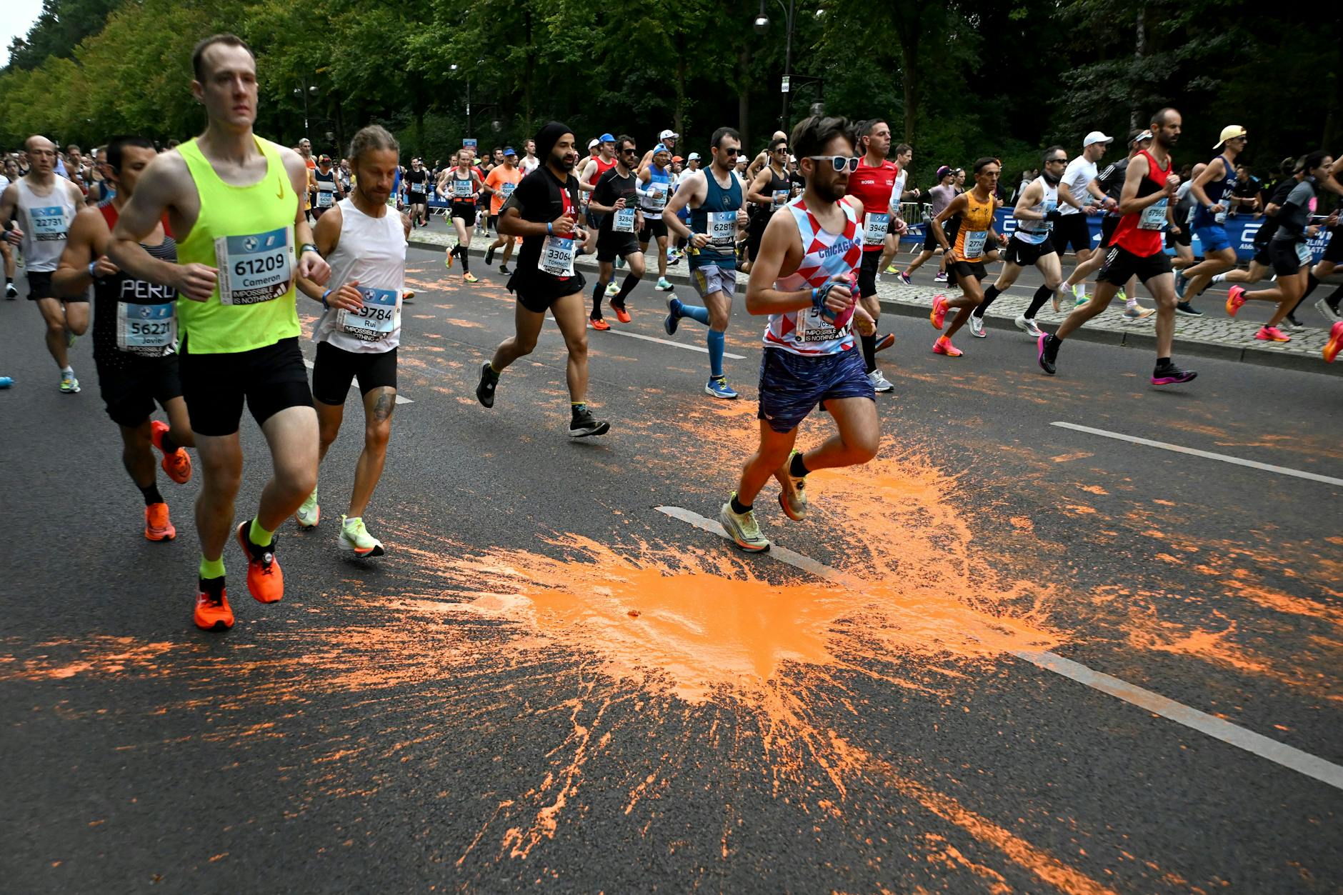 Marathonteilnehmer laufen durch die orangefarbene Farbe, die von Aktivisten der Klimaschutzgruppe Letzte Generation bei einer Protestaktion zum Marathon am 24. September 2023 in Berlin auf den Asphalt geschüttet wurde.