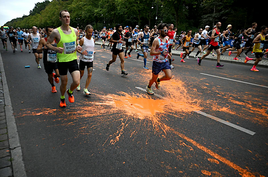 Marathonteilnehmer laufen durch die orangefarbene Farbe, die von Aktivisten der Klimaschutzgruppe Letzte Generation bei einer Protestaktion zum Marathon am 24. September 2023 in Berlin auf den Asphalt geschüttet wurde.