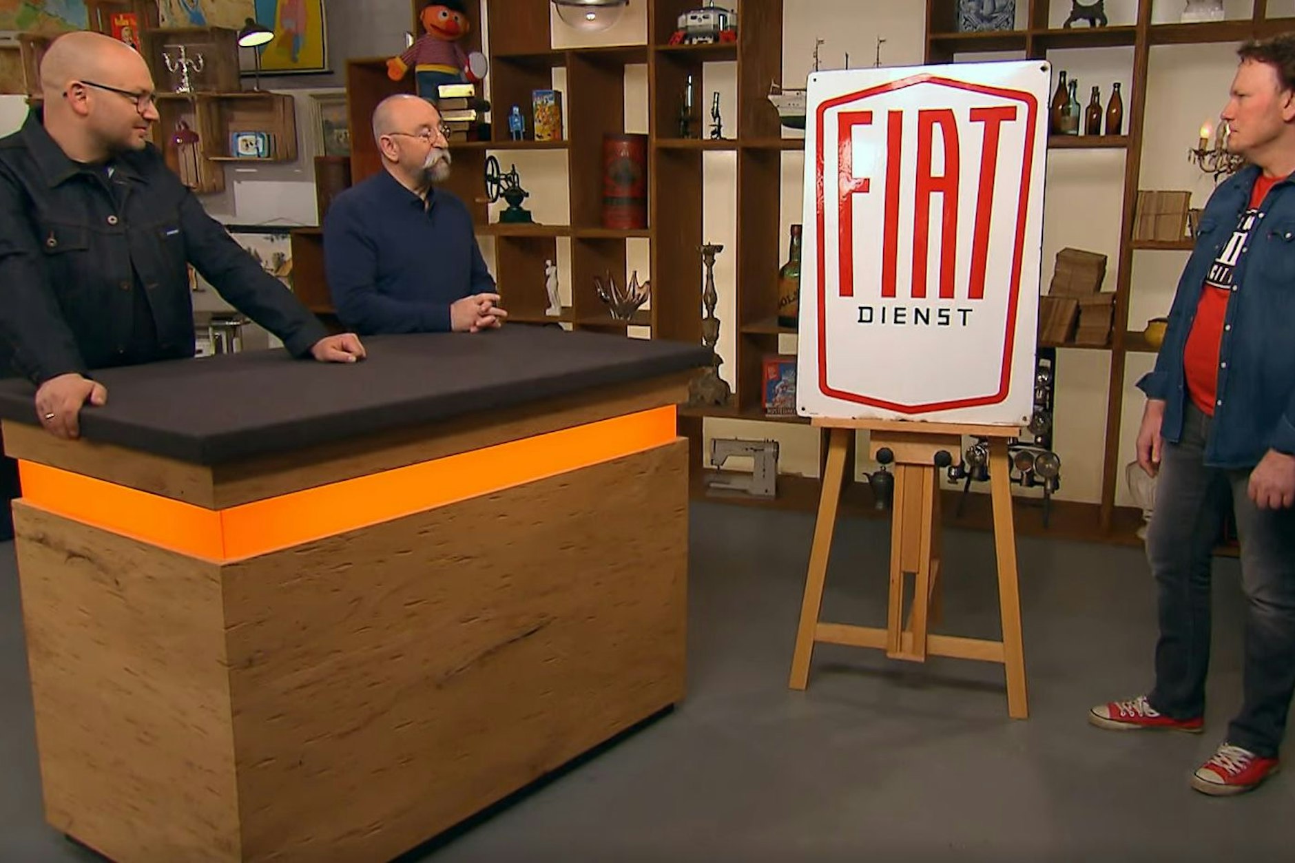 Drei Männer mit Schild: Verkäufer Jens (r.) präsentiert sein Fiat-Blech bei „Bares für Rares“-Moderator Horst Lichter und Sven Deutschmanek (l.).
