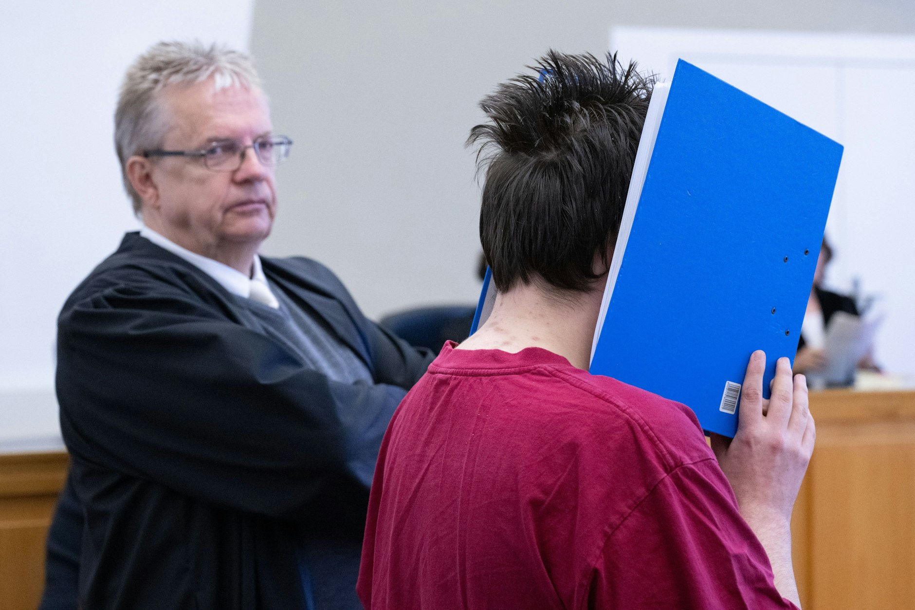Der Angeklagte Jan Heiko P. wird in den Verhandlungssaal geführt, verbirgt sein Gesicht hinter einem Aktenordner. Neben ihm steht sein Anwalt Henner Maaß.