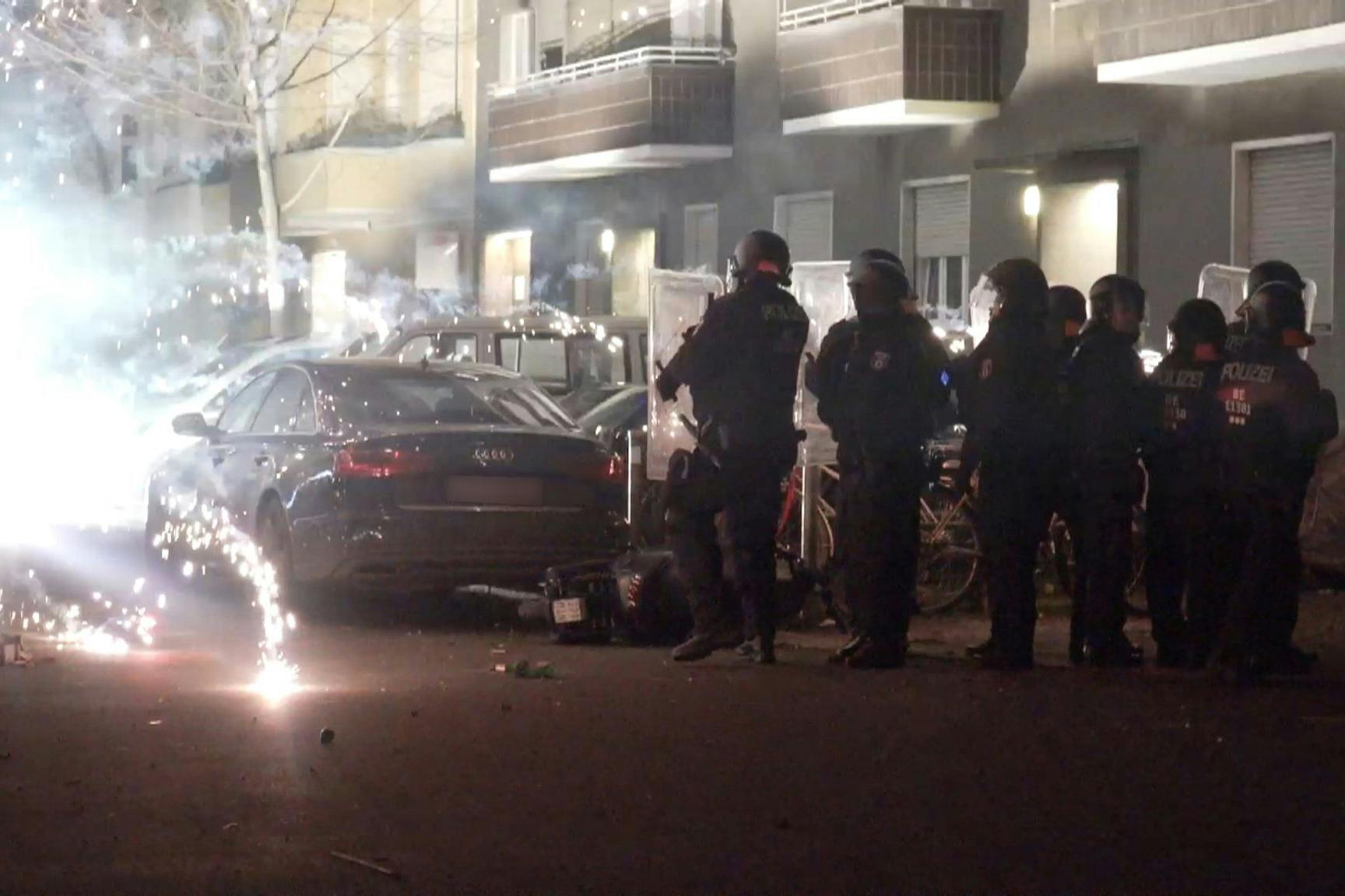 Polizeibeamte hinter explodierendem Feuerwerk in Berlin. Nach Angriffen auf Einsatzkräfte läuft die Diskussion um Konsequenzen.