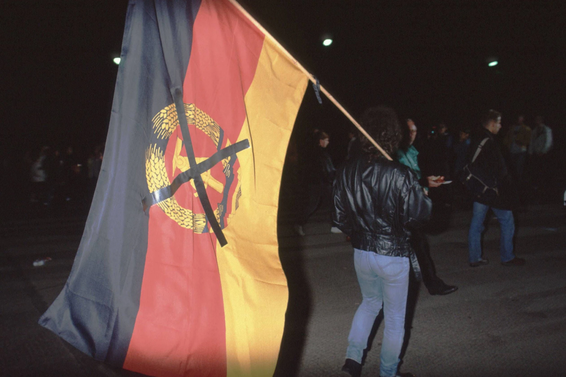 Eine Person trägt während der Deutschen Wiedervereinigung eine durchgestrichene DDR-Flagge.