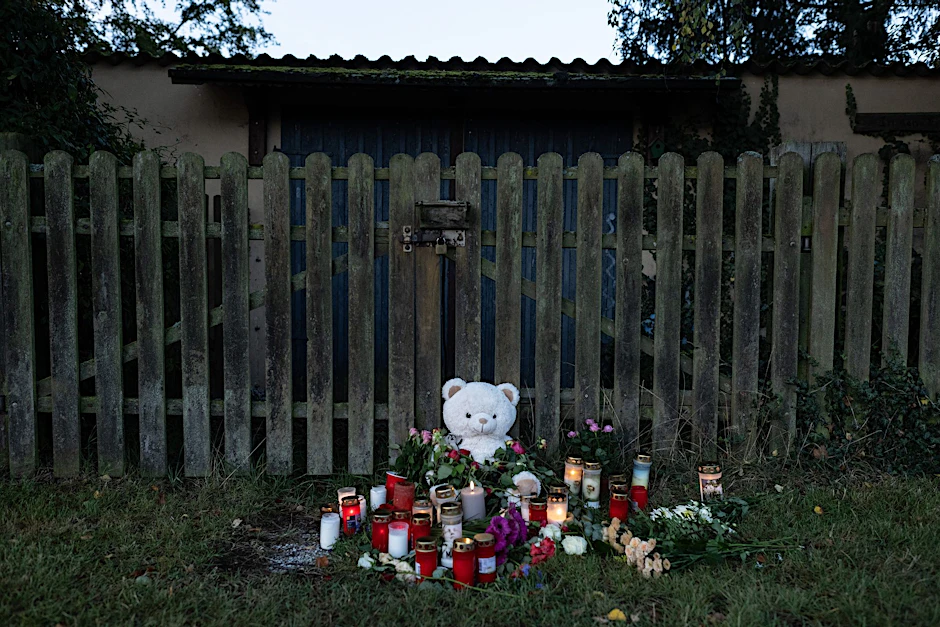 Kerzen, Blumen und ein großer Plüschteddy vor einem Zaun am Fundort der Leiche einer 14-Jährigen.  
