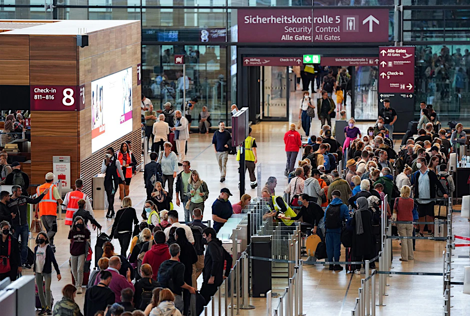Reisende warten auf dem Flughafen BER auf die Sicherheitskontrolle.