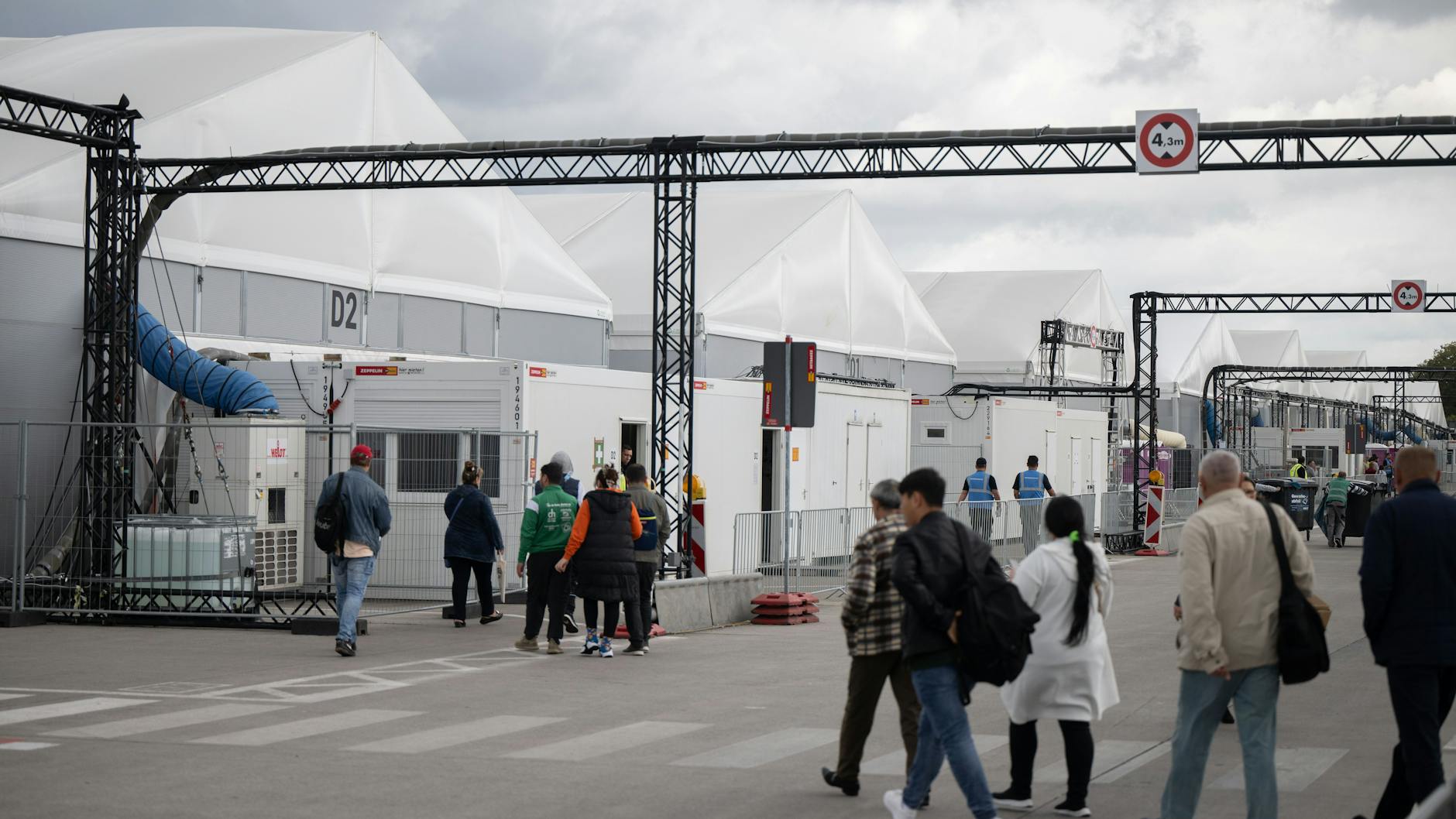 Bewohner und Mitarbeiter gehen im Ankunftszentrum am ehemaligen Flughafen Tegel in Richtung der Leichtbauhallen.