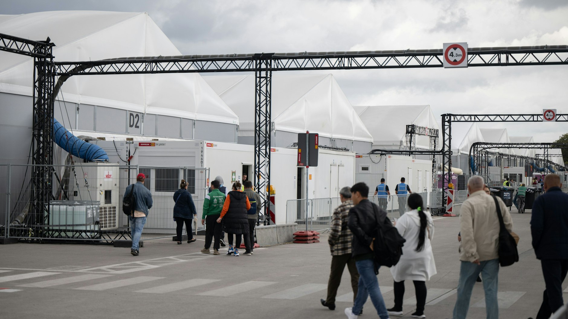 Bewohner und Mitarbeiter gehen im Ankunftszentrum am ehemaligen Flughafen Tegel in Richtung der Leichtbauhallen.