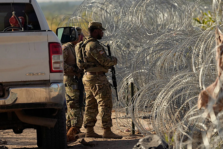 Soldaten stehen neben einem Stacheldrahtzaun am Ufer des Rio Grande Wache.  