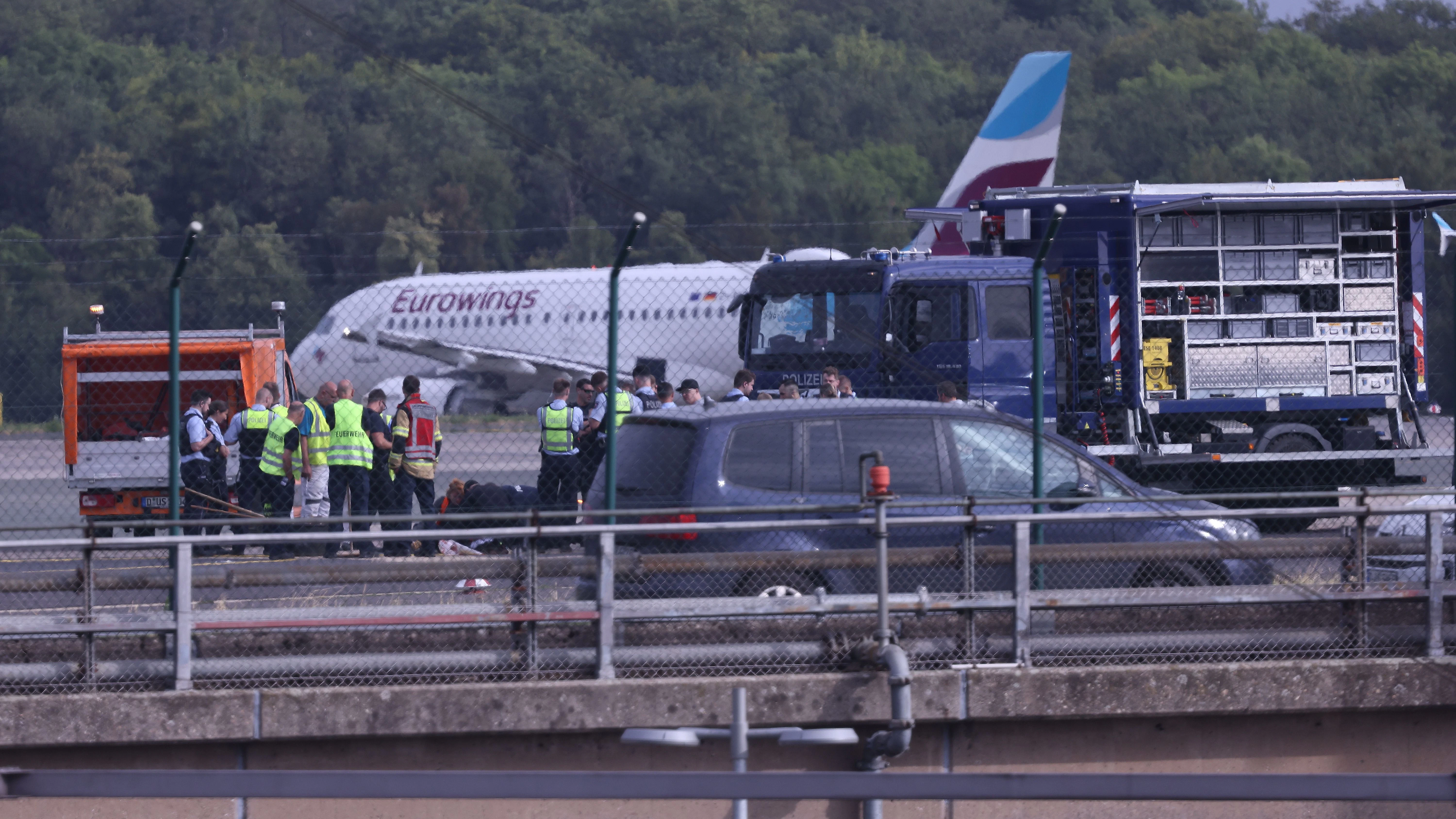 Im Juli stehen Sicherheitspersonal und Polizisten stehen auf dem Flugfeld in Düsseldorf und versuchen Aktivisten der Gruppe Letzte Generation vom Asphalt zu lösen, die eine Eurowings-Maschine blockieren.