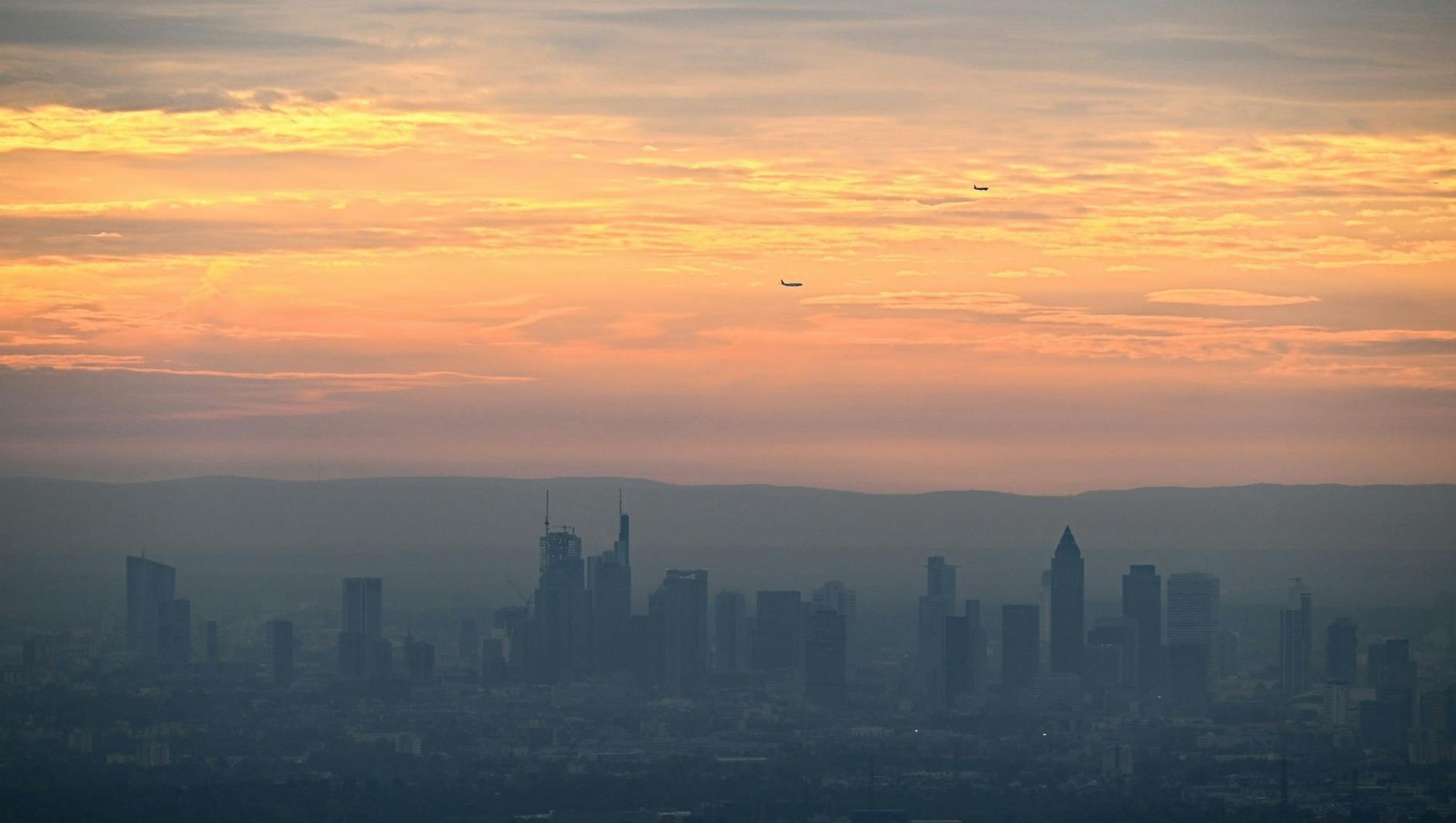 Ein perfektes Postkarten-Motiv aus Frankfurt am Main: Während die Hochhäuser bei Sonnenaufgang im Dunst liegen, ist der Himmel orange verfärbt.