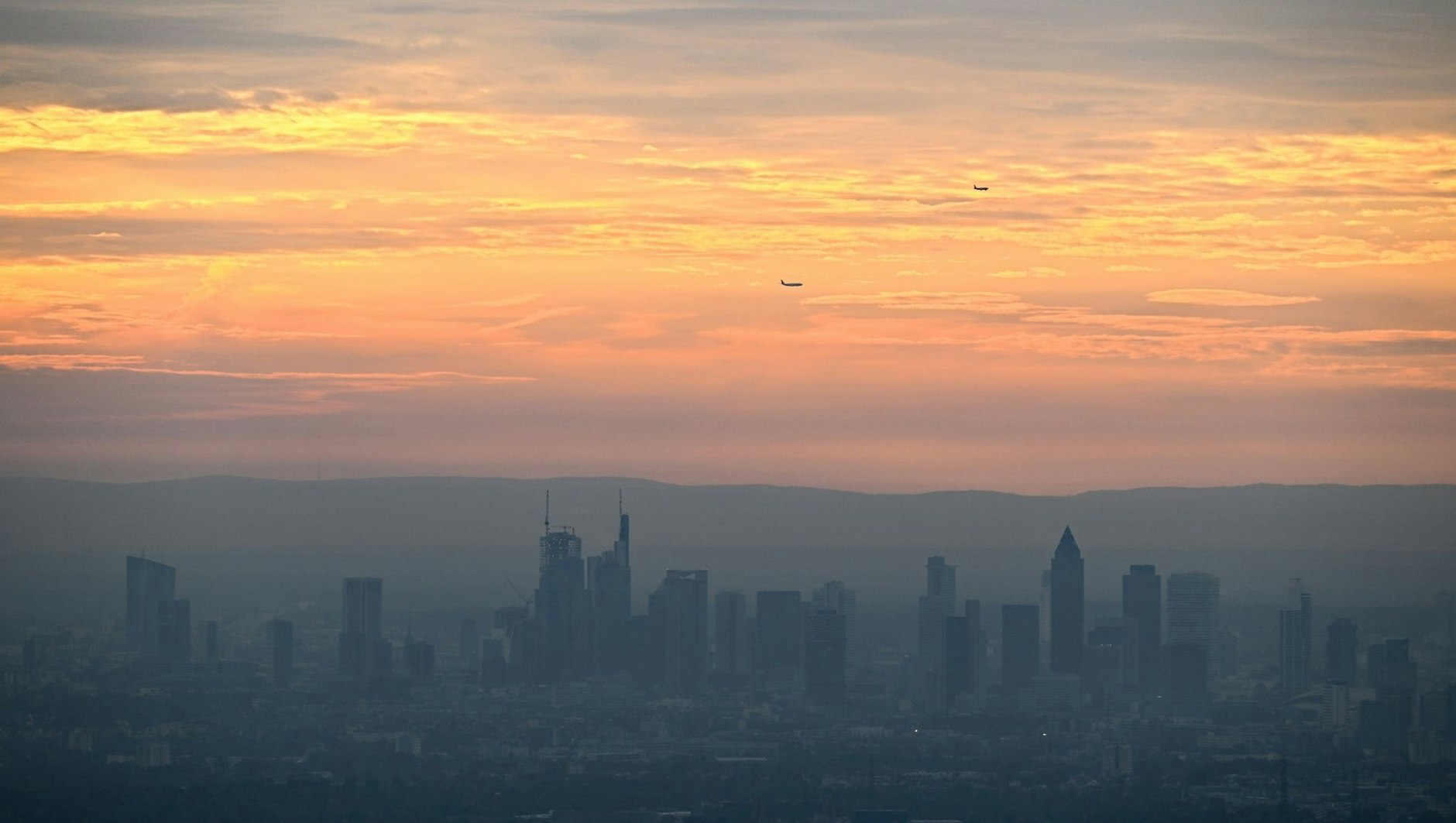 Ein perfektes Postkarten-Motiv aus Frankfurt am Main: Während die Hochhäuser bei Sonnenaufgang im Dunst liegen, ist der Himmel orange verfärbt.  